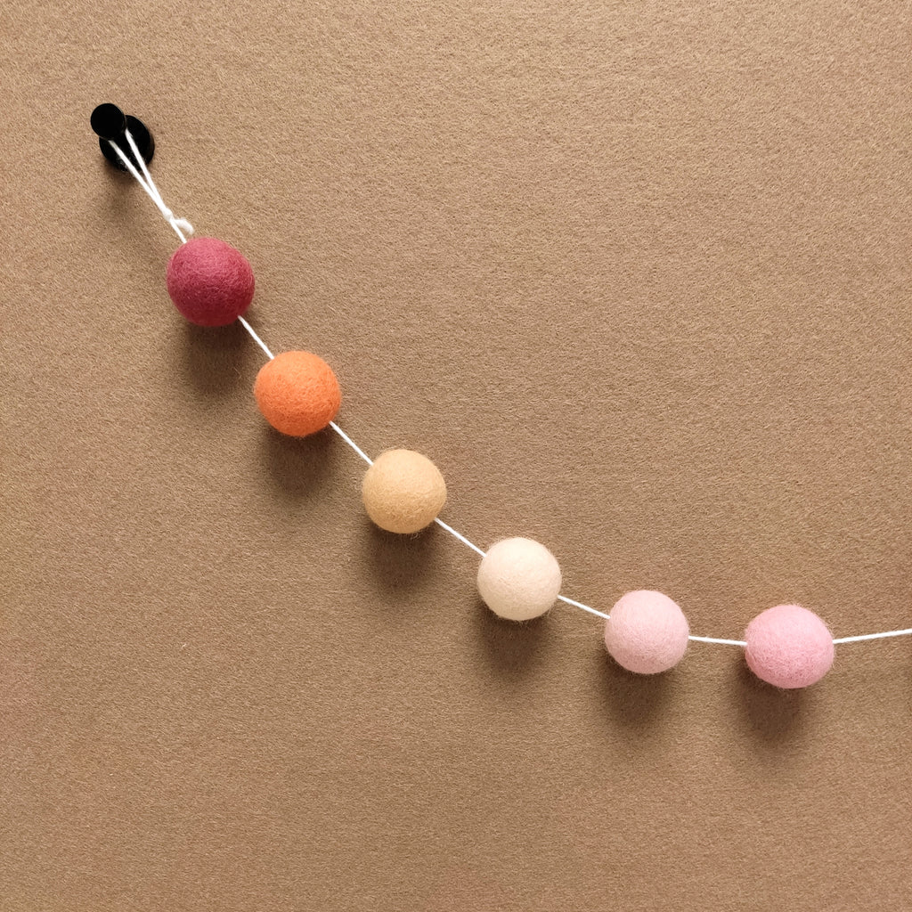 Zoom sur les 6 couleurs de la guirlande de pompons beige rosé, orange pêche, orange flamingo, rose poudré, rose cerisier, rose boisé
