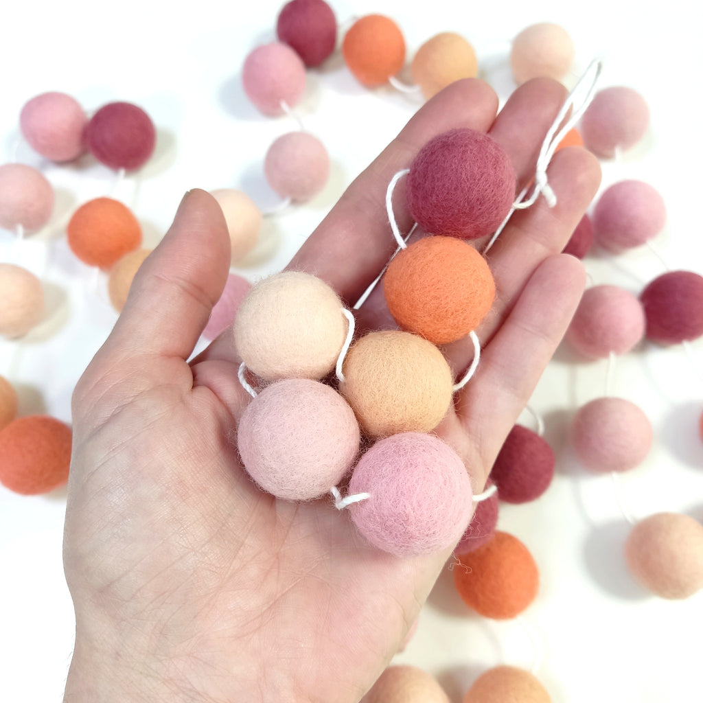 Détail des pompons de feutre de 2,5 cm de la guirlande rose pêche dans une main