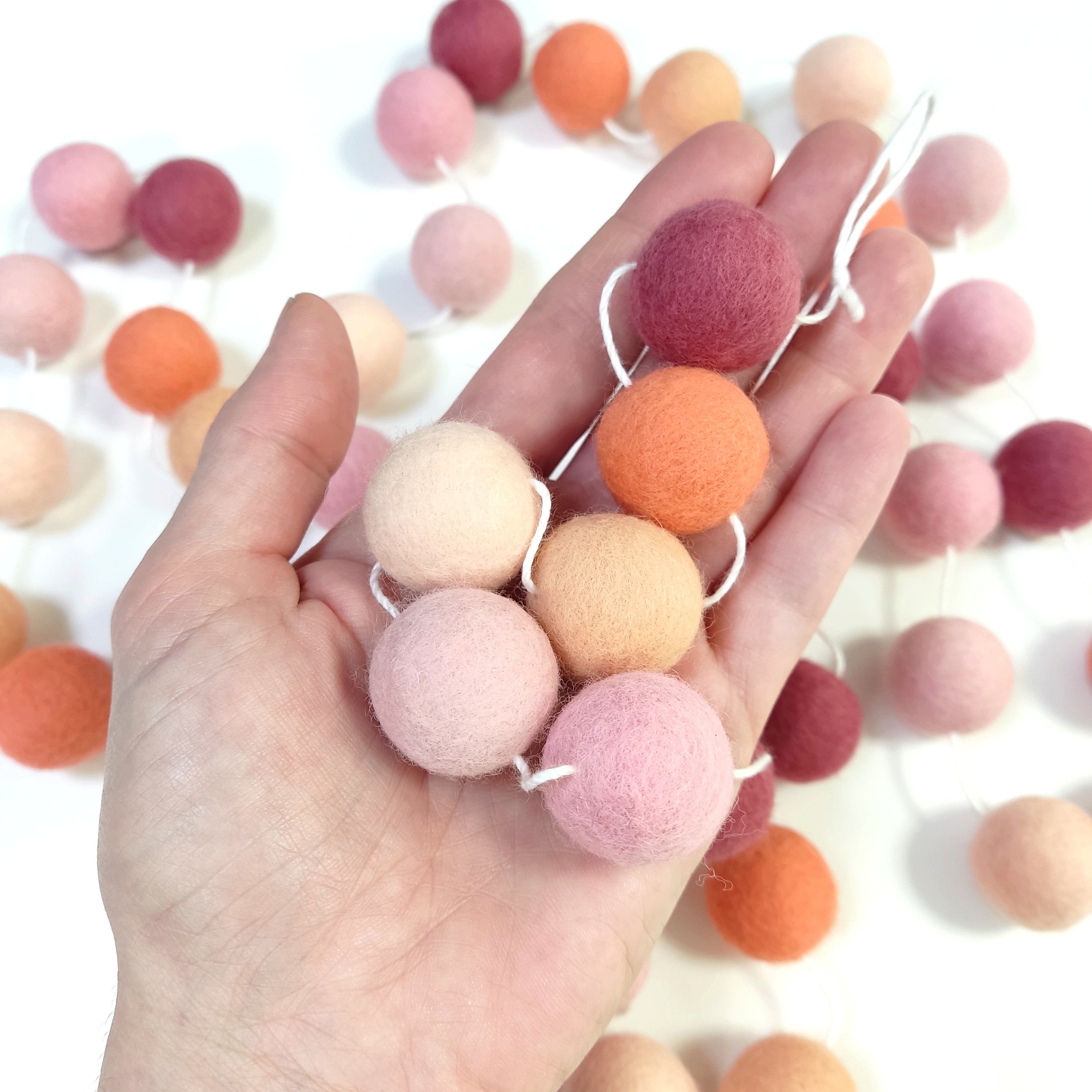 Détail des pompons de feutre de 2,5 cm de la guirlande rose pêche dans une main