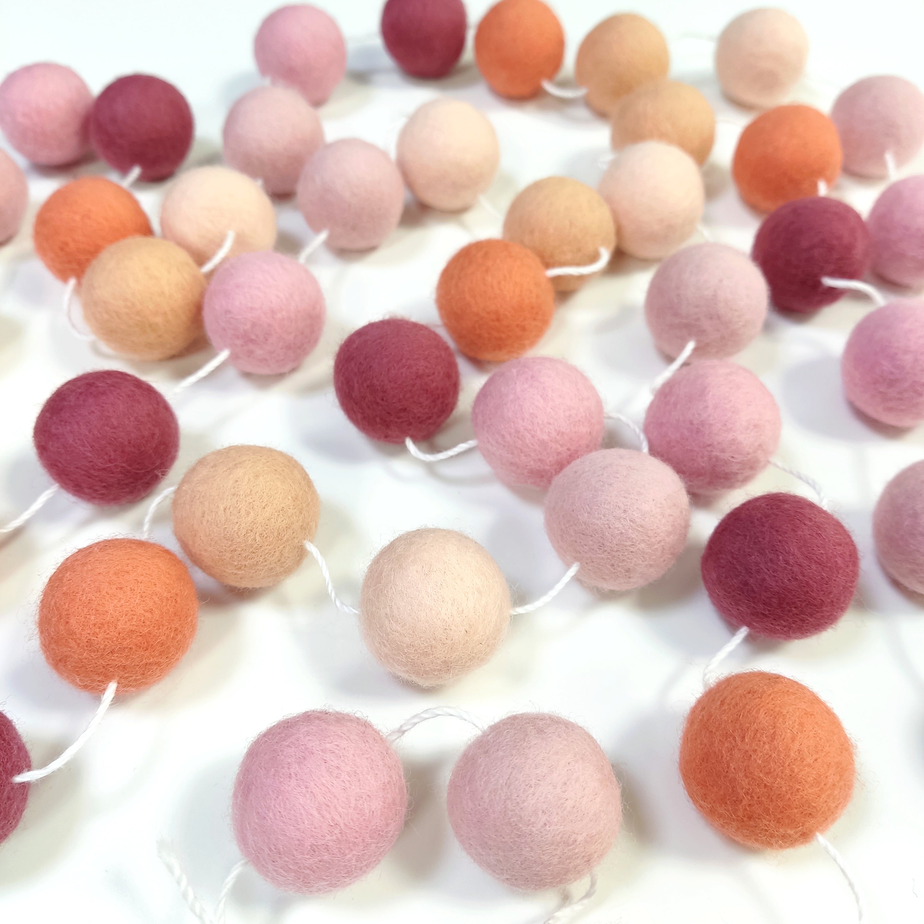 Guirlande de boules de laine feutrée rose pêche étalée sur une table avec les pompons espacés