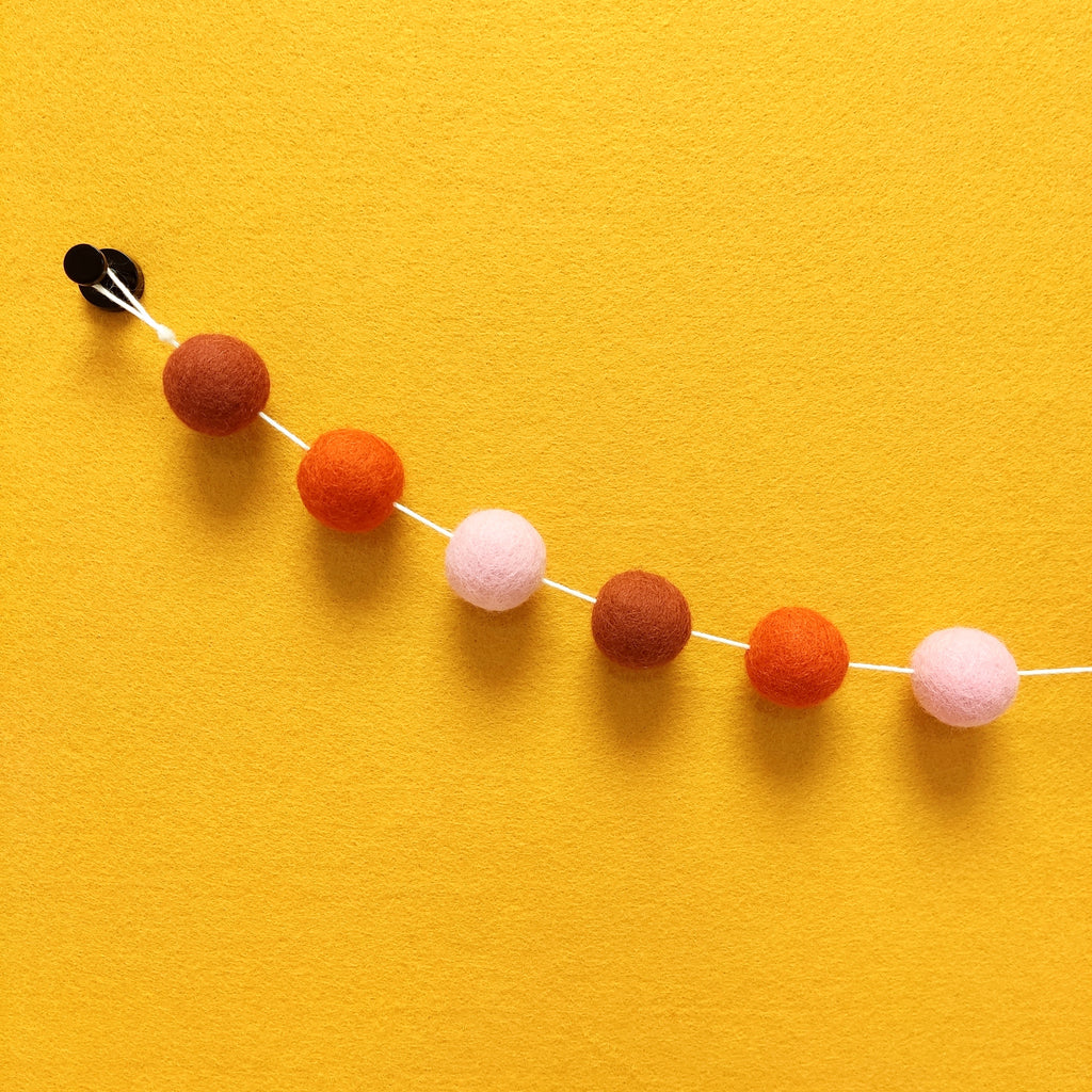 Détail des 3 couleurs de pompons feutrés terracotta rouge, orange mandarine et rose poudré de la guirlande Pétale Terracotta