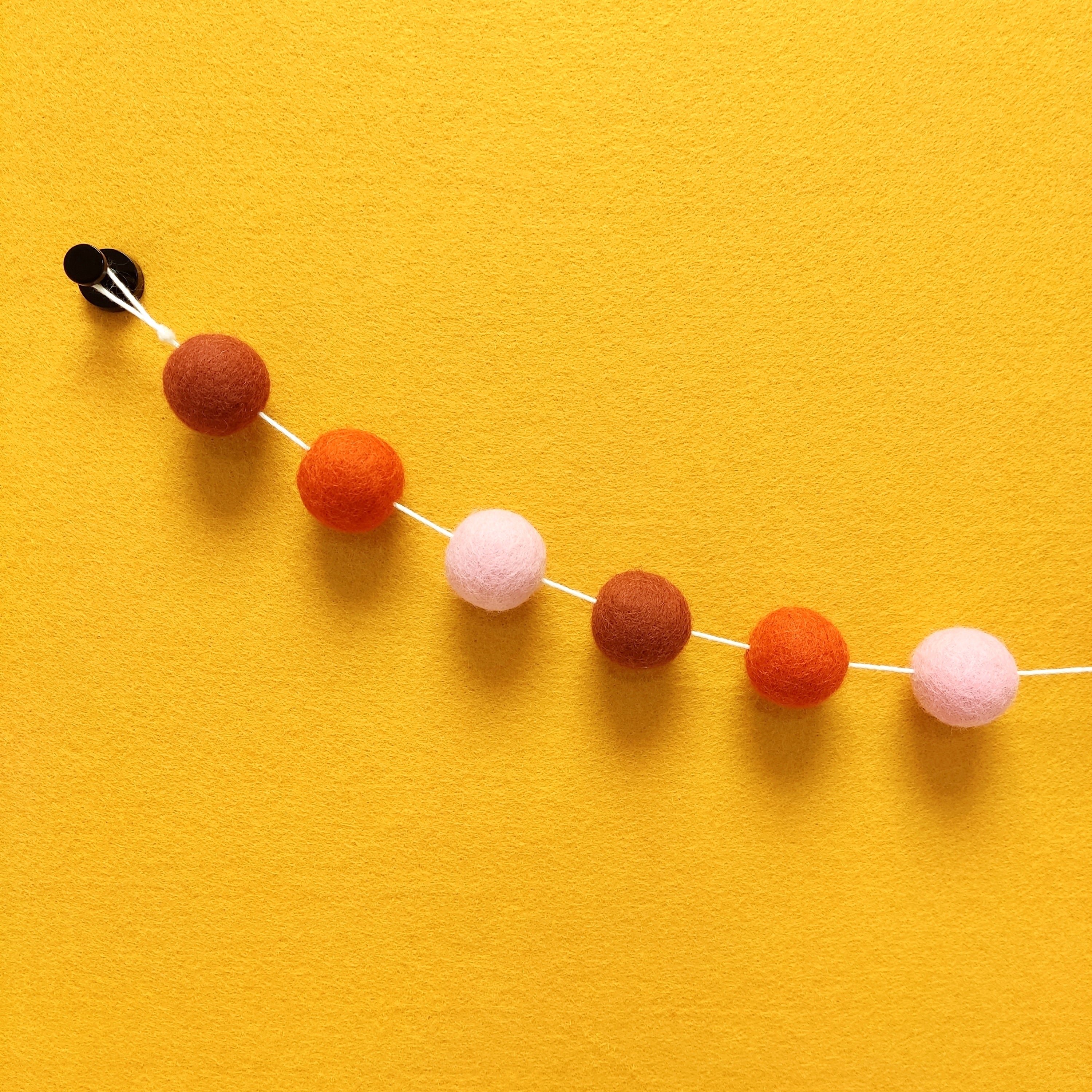Détail des 3 couleurs de pompons feutrés terracotta rouge, orange mandarine et rose poudré de la guirlande Pétale Terracotta