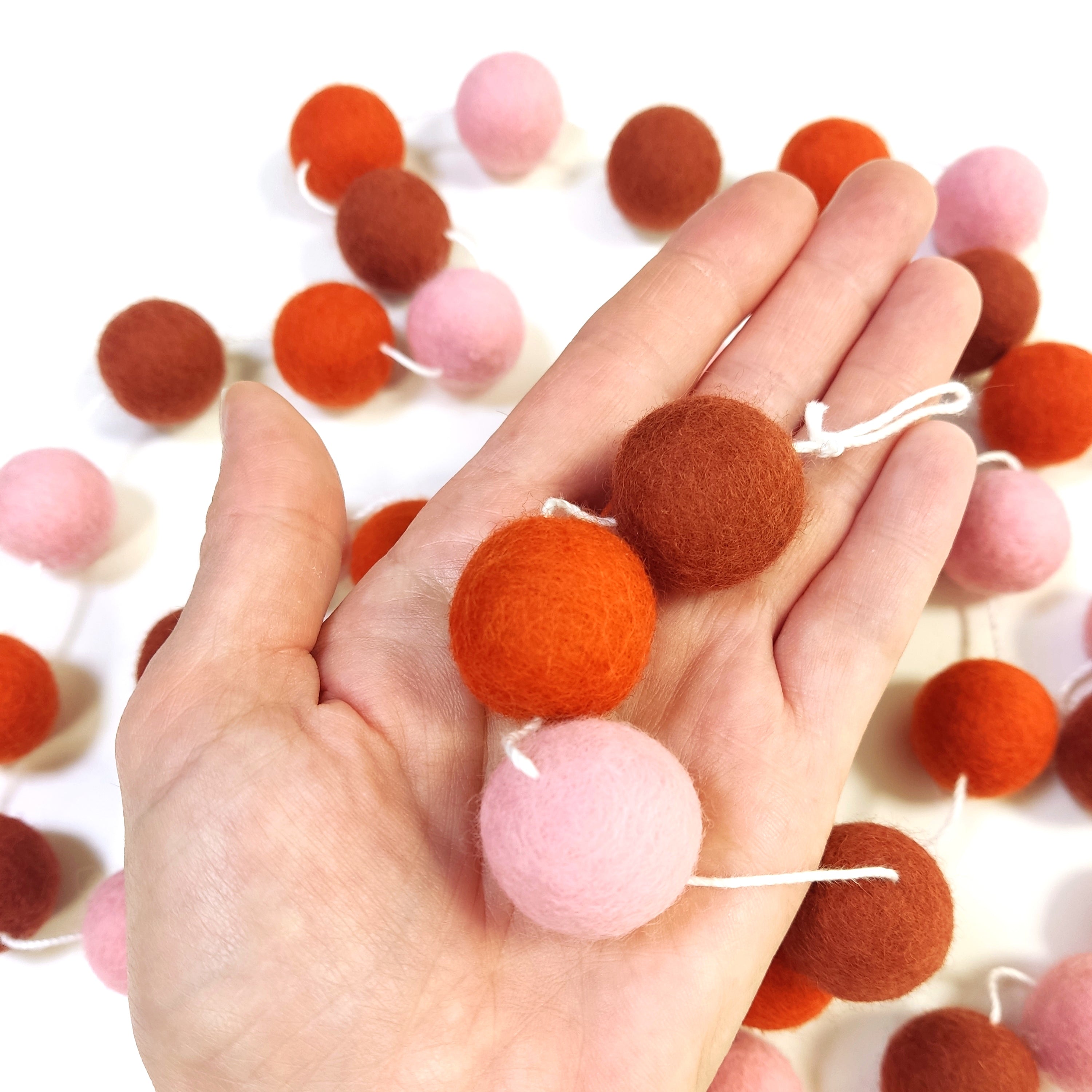 Zoom sur les pompons en laine mérinos pétale terracotta dans une main, teintes chaudes et naturelles