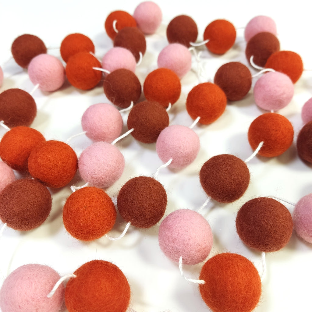 Guirlande de pompons feutrés pétale terracotta étalée sur une table avec les pompons espacés sur le fil