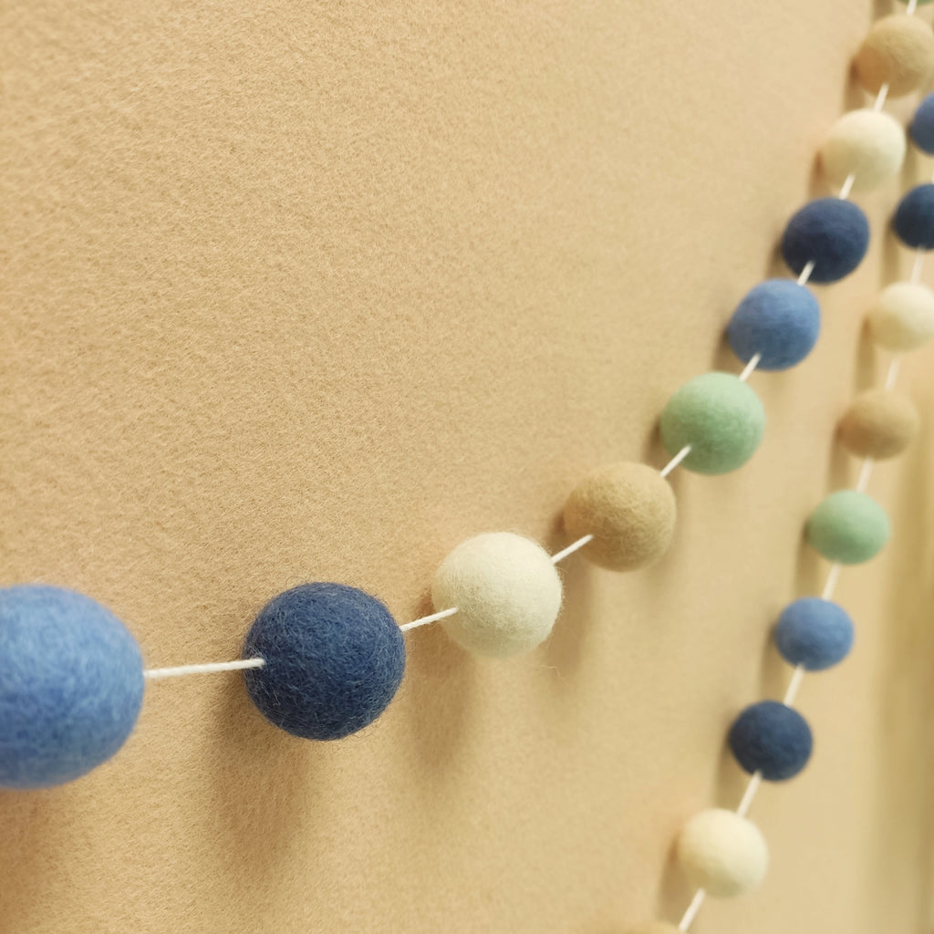 Guirlande en boules de feutre tons bleu vert beige blanc vue de profil sur un mur