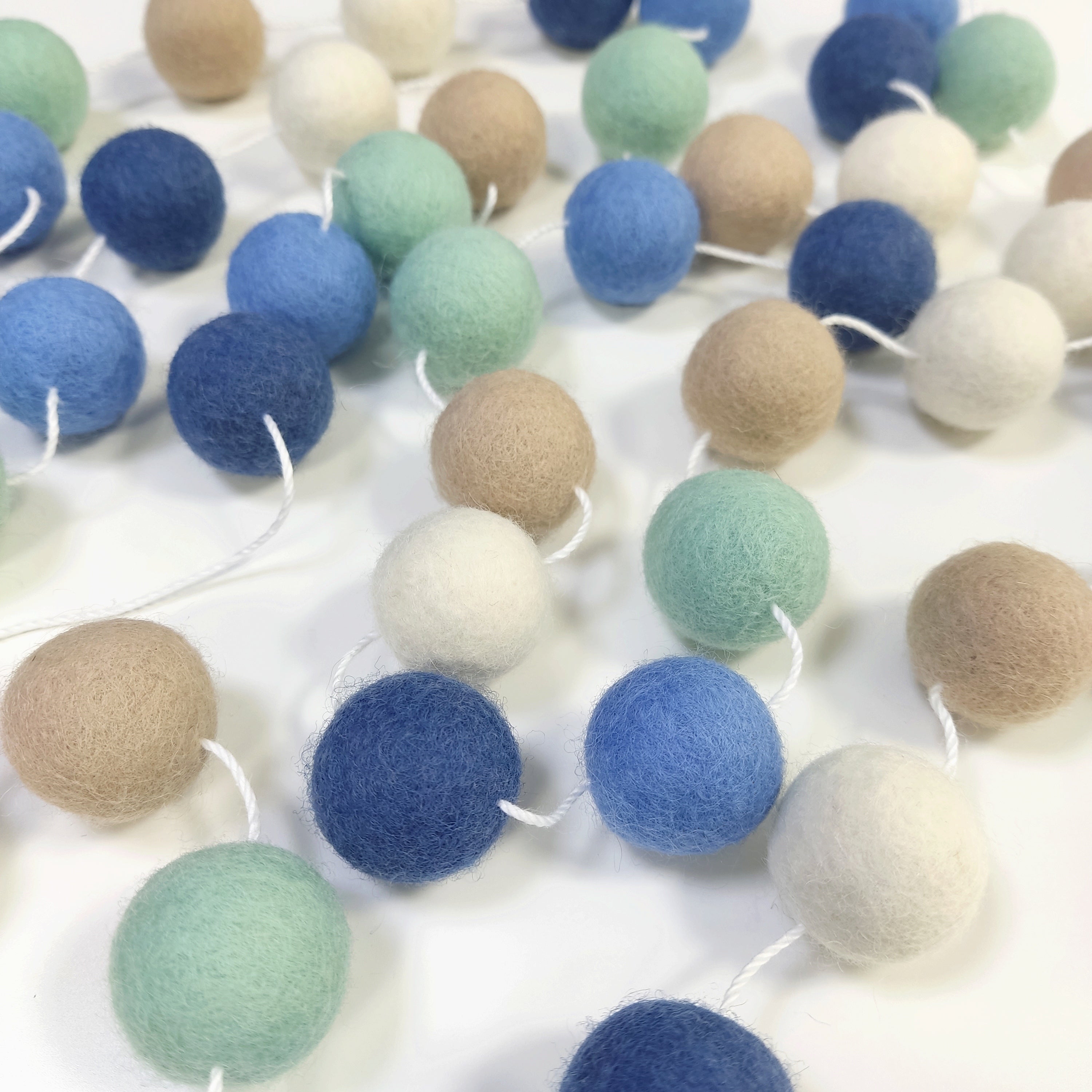 Guirlande de boule de laine feutrée riviera étalée sur une table avec les pompons espacés