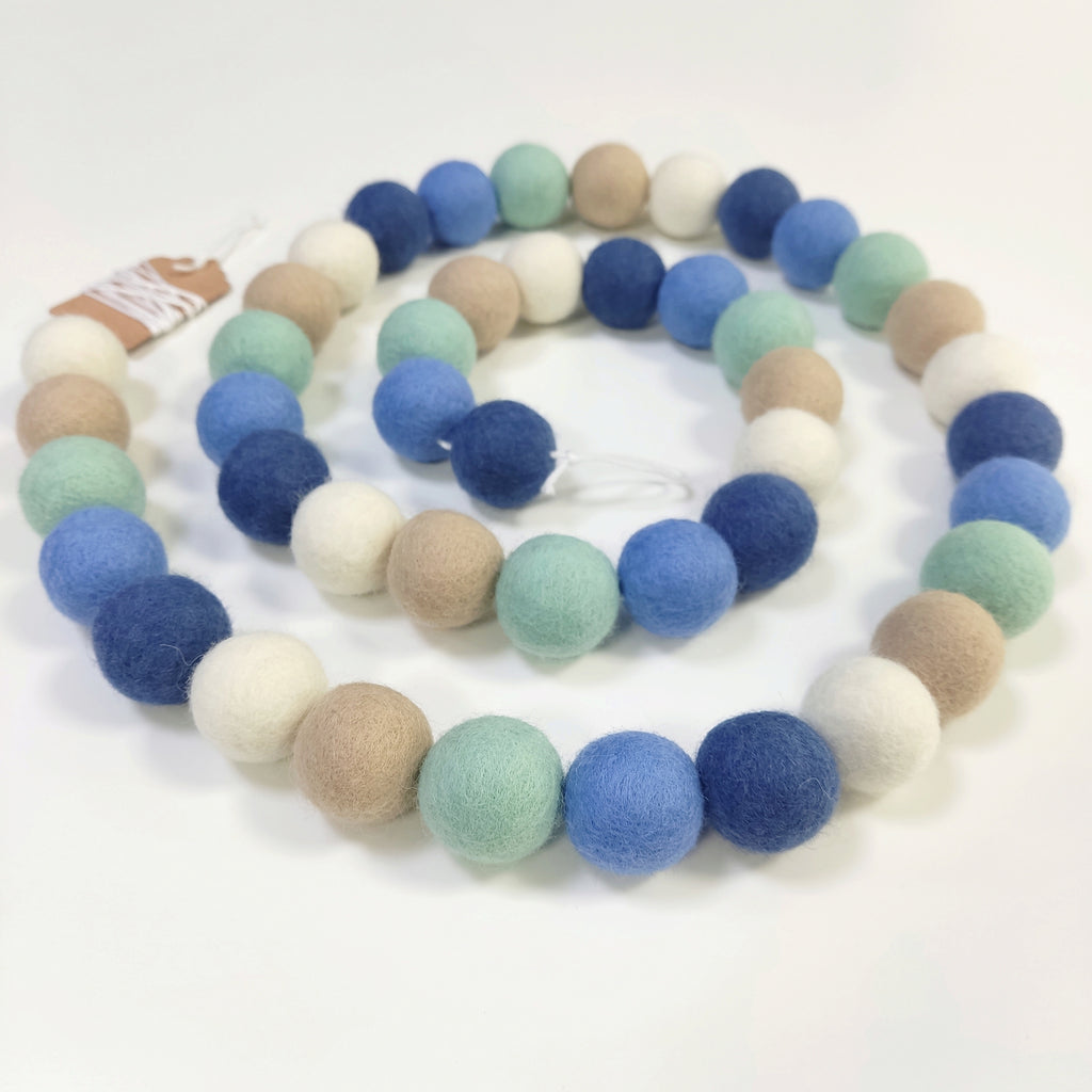 Guirlande de pompons en feutre blanc, beige, bleu chambray, vert menthe et bleu denim disposée en spirale vue de dessus