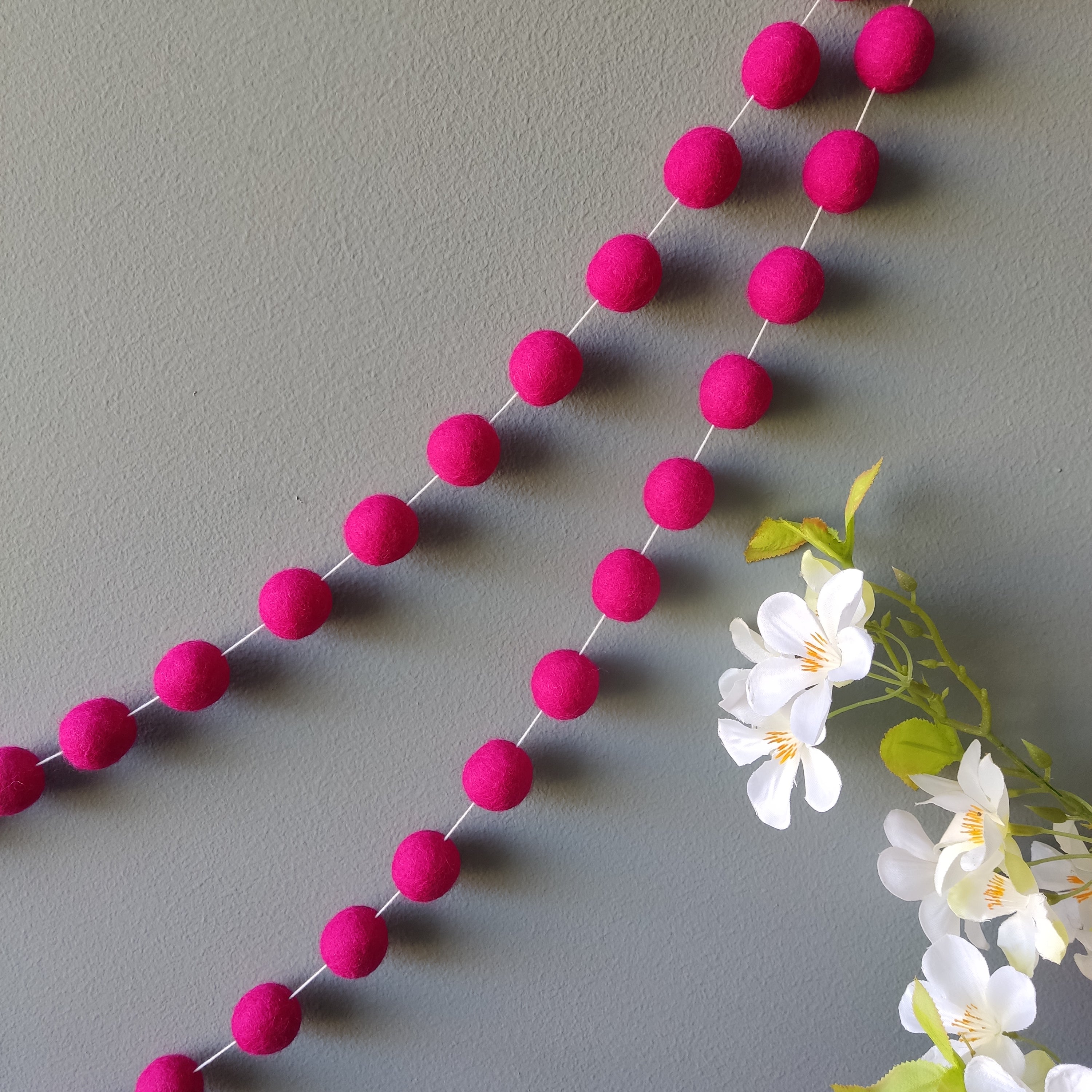 Guirlande de pompons feutrés rose magenta pour fête ou décoration chambre fille accrochée sur un mur