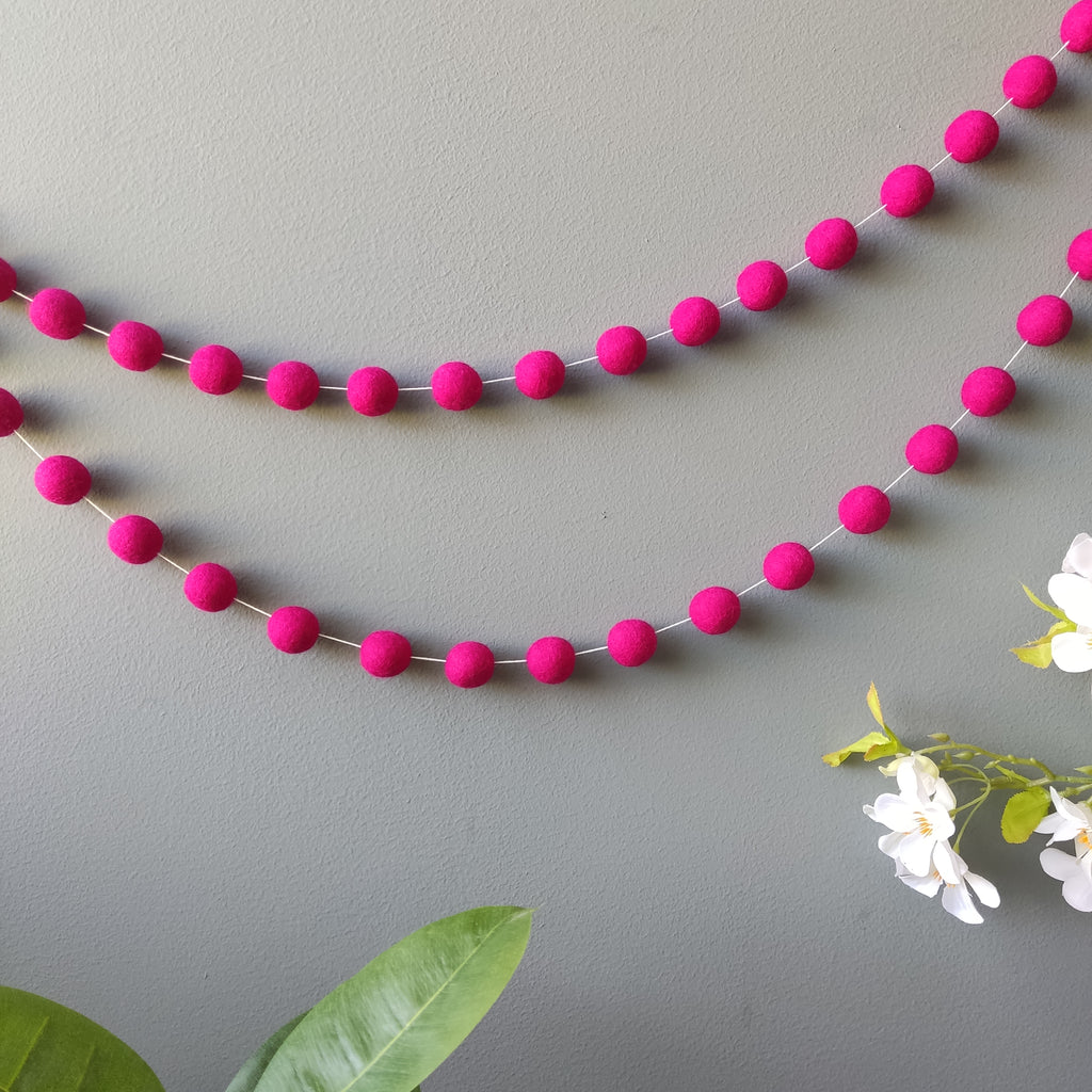 Guirlande de pompons roses vue de loin sur un mur