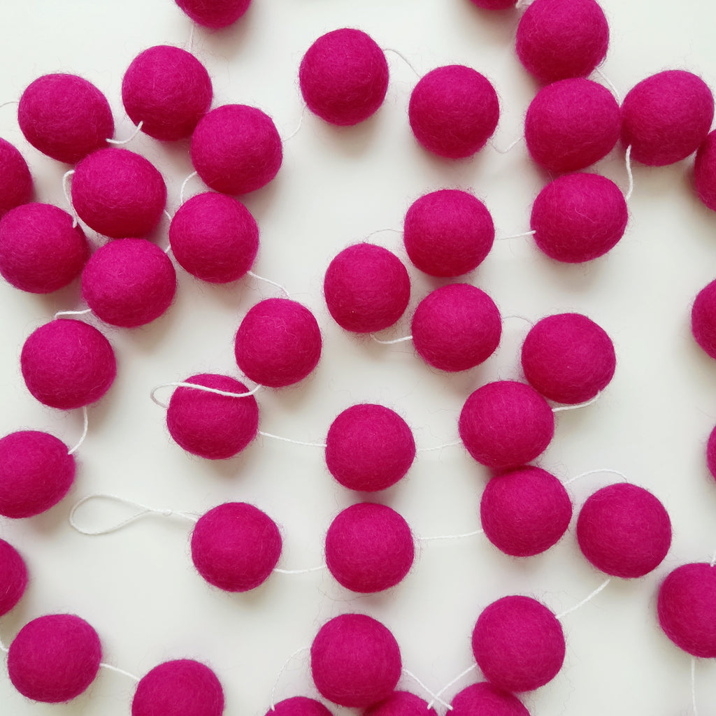 Pompons de laine mérinos feutrés de la guirlande rose magenta étalés sur une table