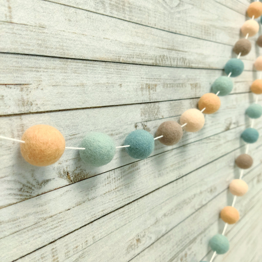 Guirlande de pompons feutrés aux teintes naturelles sauge, pêche et beige vue de profil