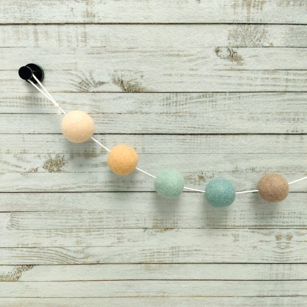 Détail des 5 couleurs de pompons feutrés beige rosé, orange pêche, beige cappuccino, bleu nordique et vert céladon