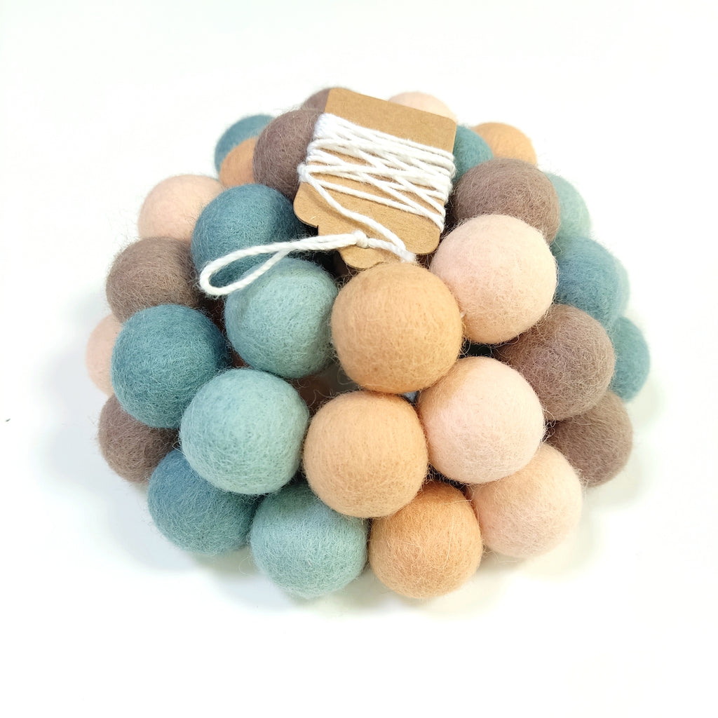 Zoom sur la guirlande de pompons en laine mérinos sauge pêche avec étiquette CELAINEDECO