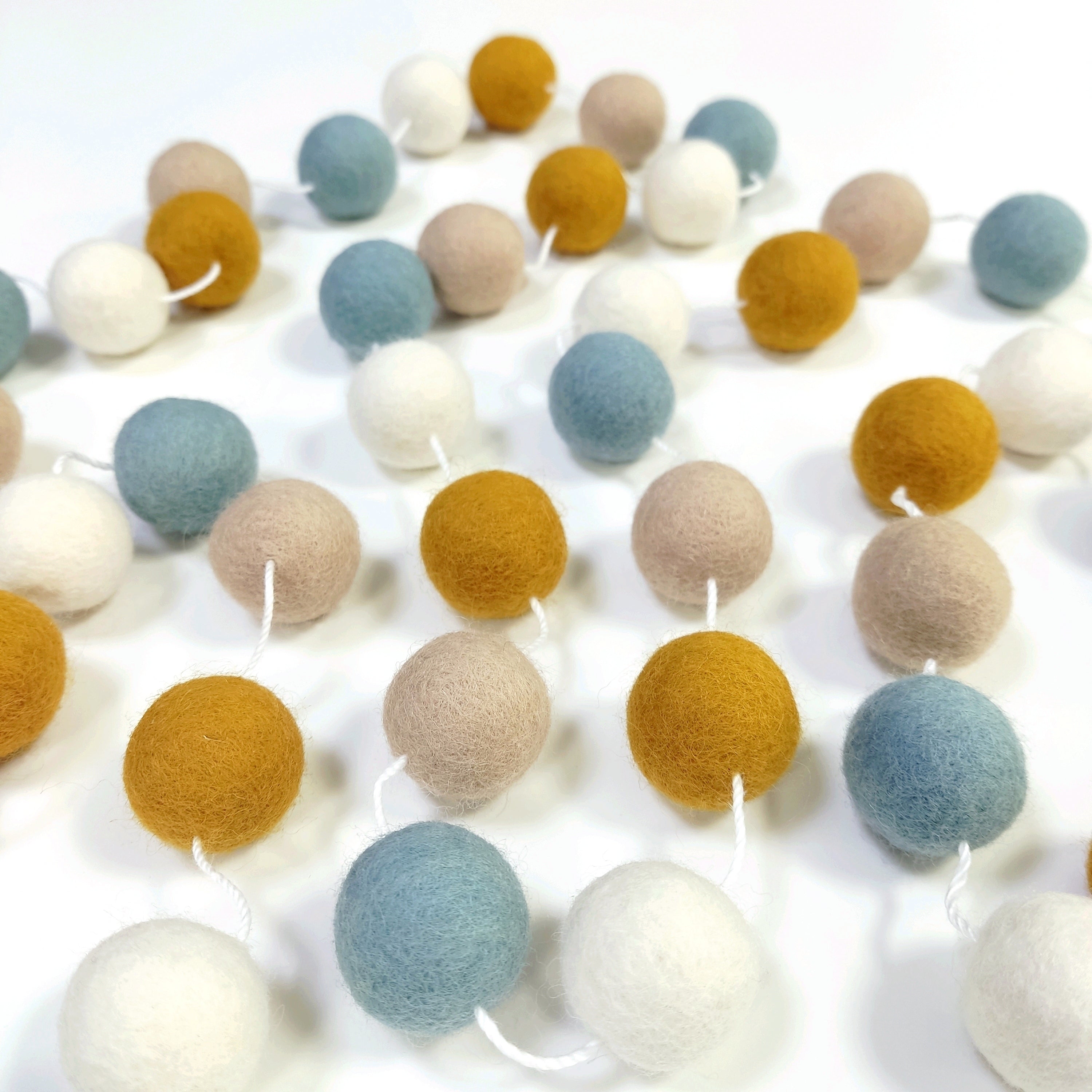 Guirlande en boules de feutre ocre bleu blanc beige posée sur une table avec les pompons espacés