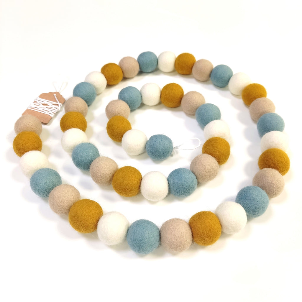 Guirlande de pompons en feutre bleu blanc ocre beige disposée en spirale vue de dessus