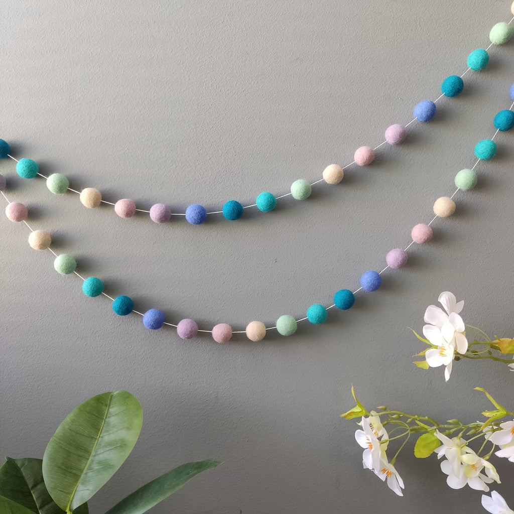Guirlande de pompons dégradé sirène fixée sur un mur