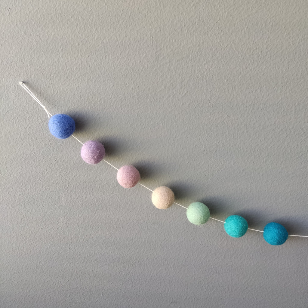 Zoom sur les pompons mauve, lilas, turquoise, beige, bleu et vert canard de la guirlande en boules de feutre sirène