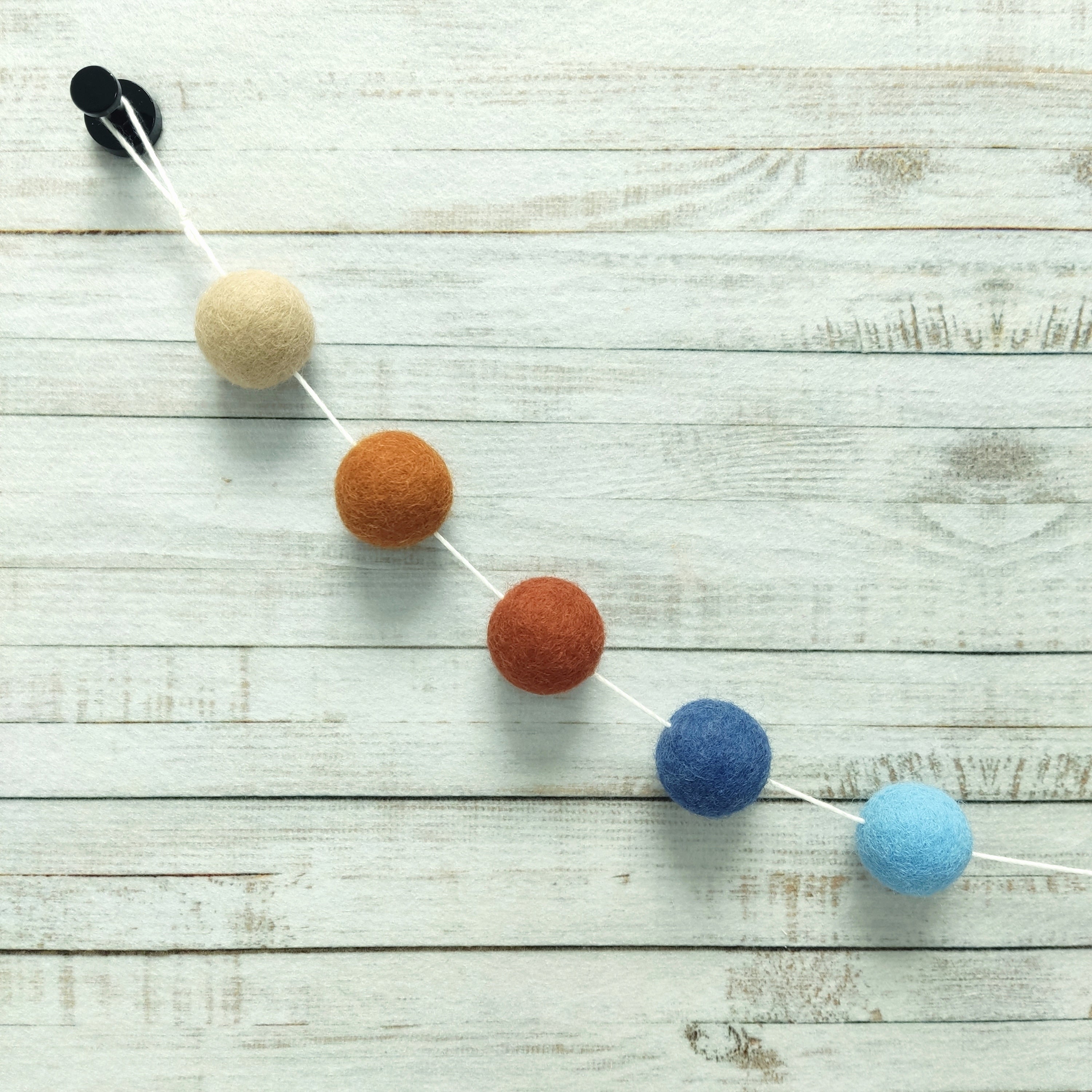 Détail des pompons feutrés beige poudré, terracotta cuivre, terracotta rouge, bleu denim et bleu ciel de la guirlande avec sa boucle de fixation