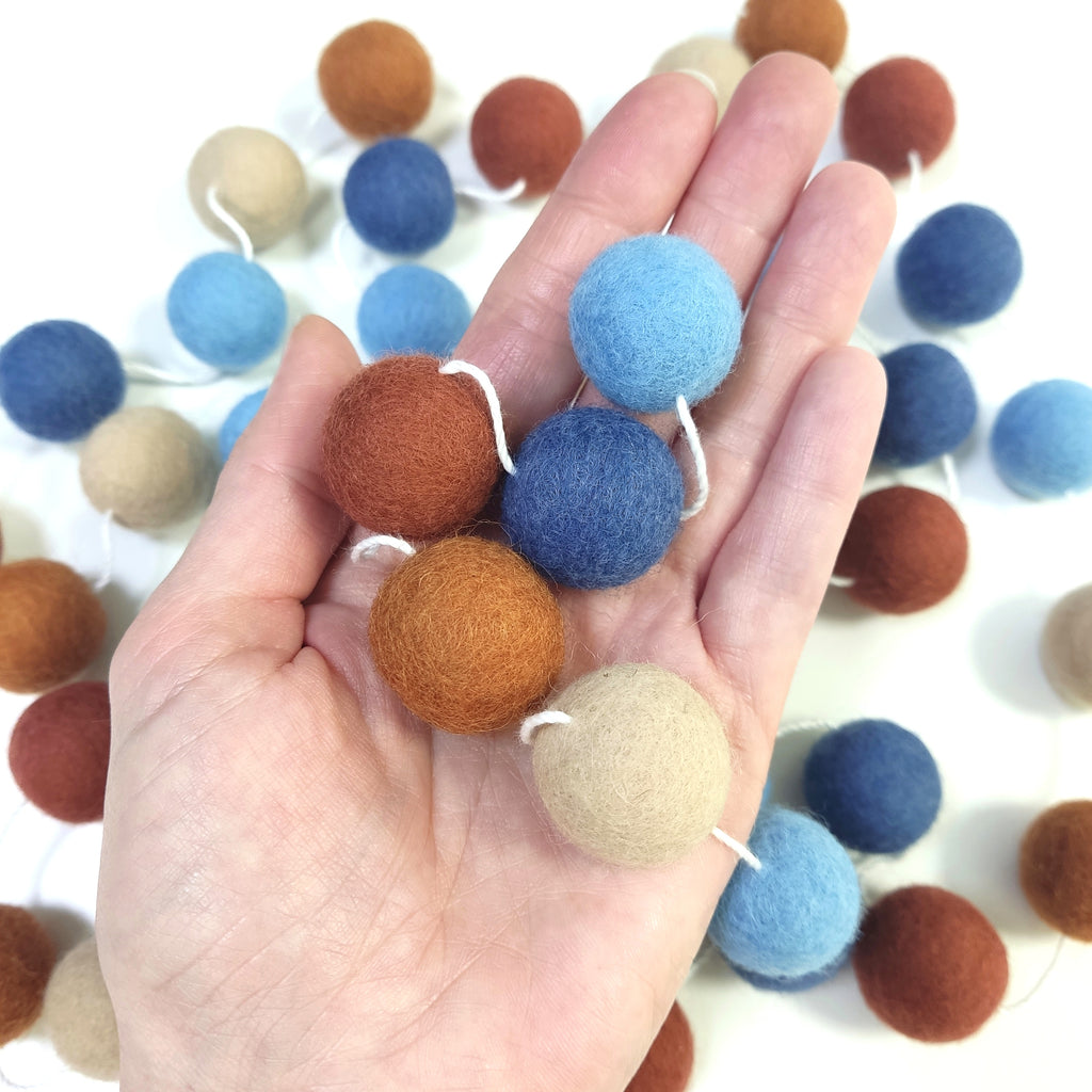 Zoom des pompons de feutre de 2,5 cm de la guirlande terracotta bleu dans une main