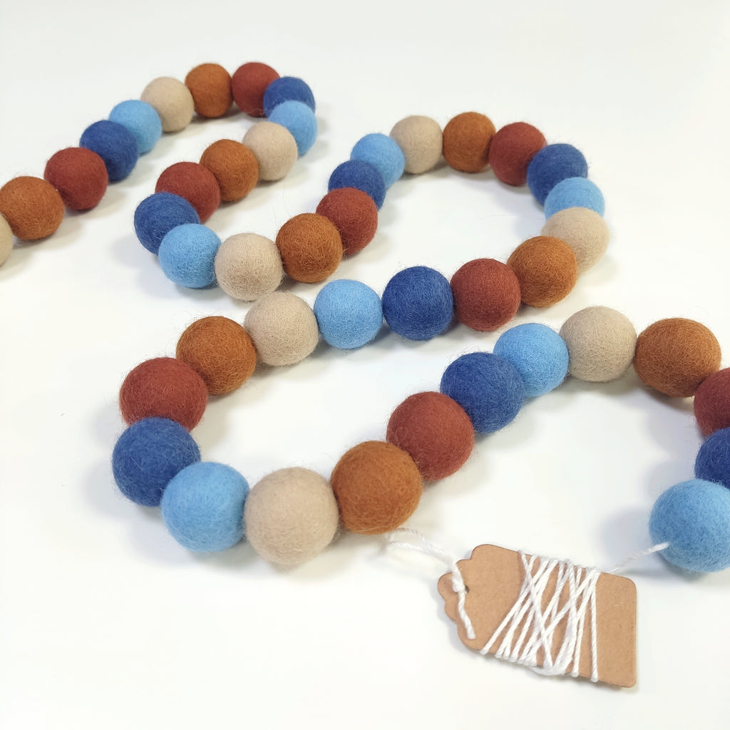 Guirlande terracotta bleu en boules de laine feutrée disposée en serpentin sur une table