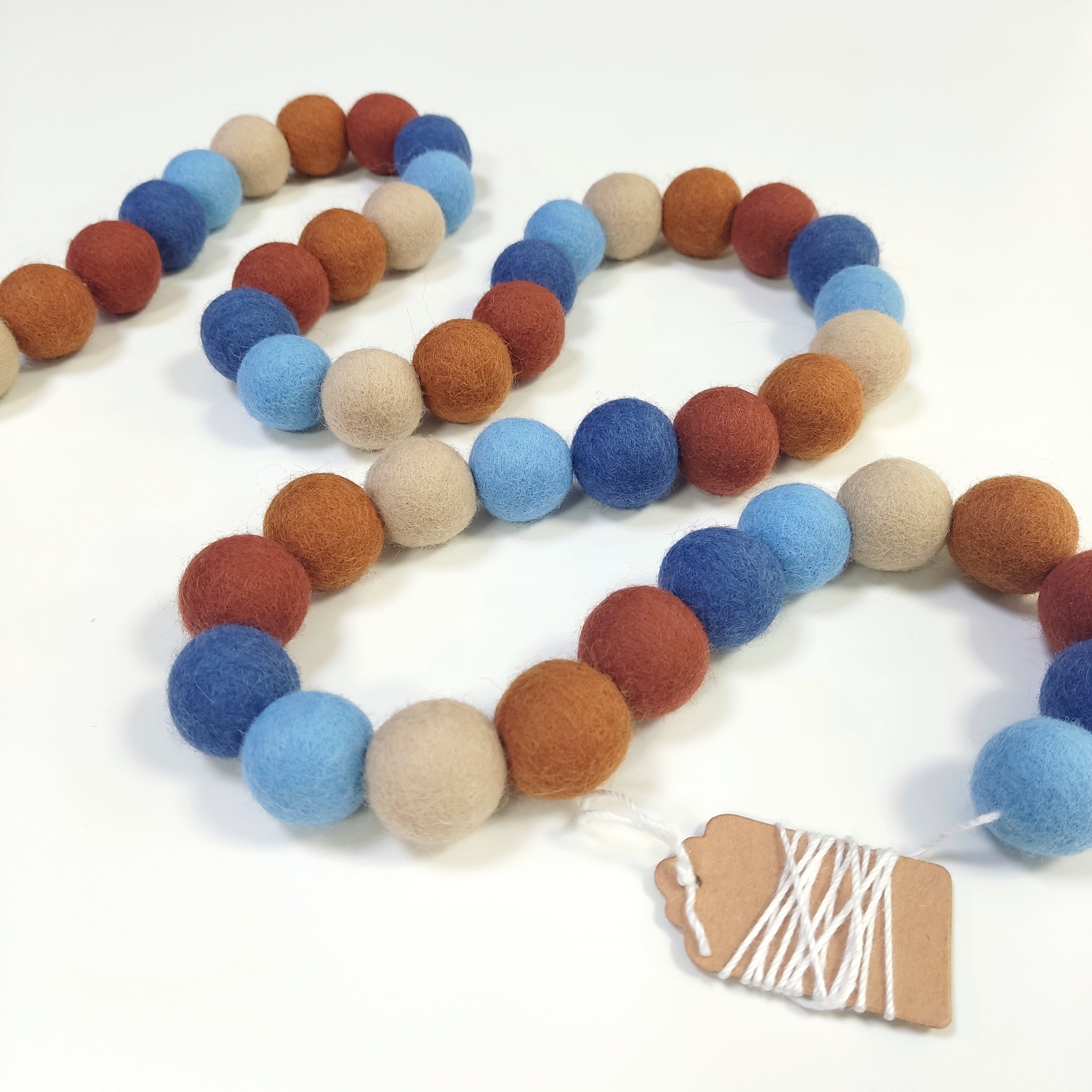 Guirlande terracotta bleu en boules de laine feutrée disposée en serpentin sur une table