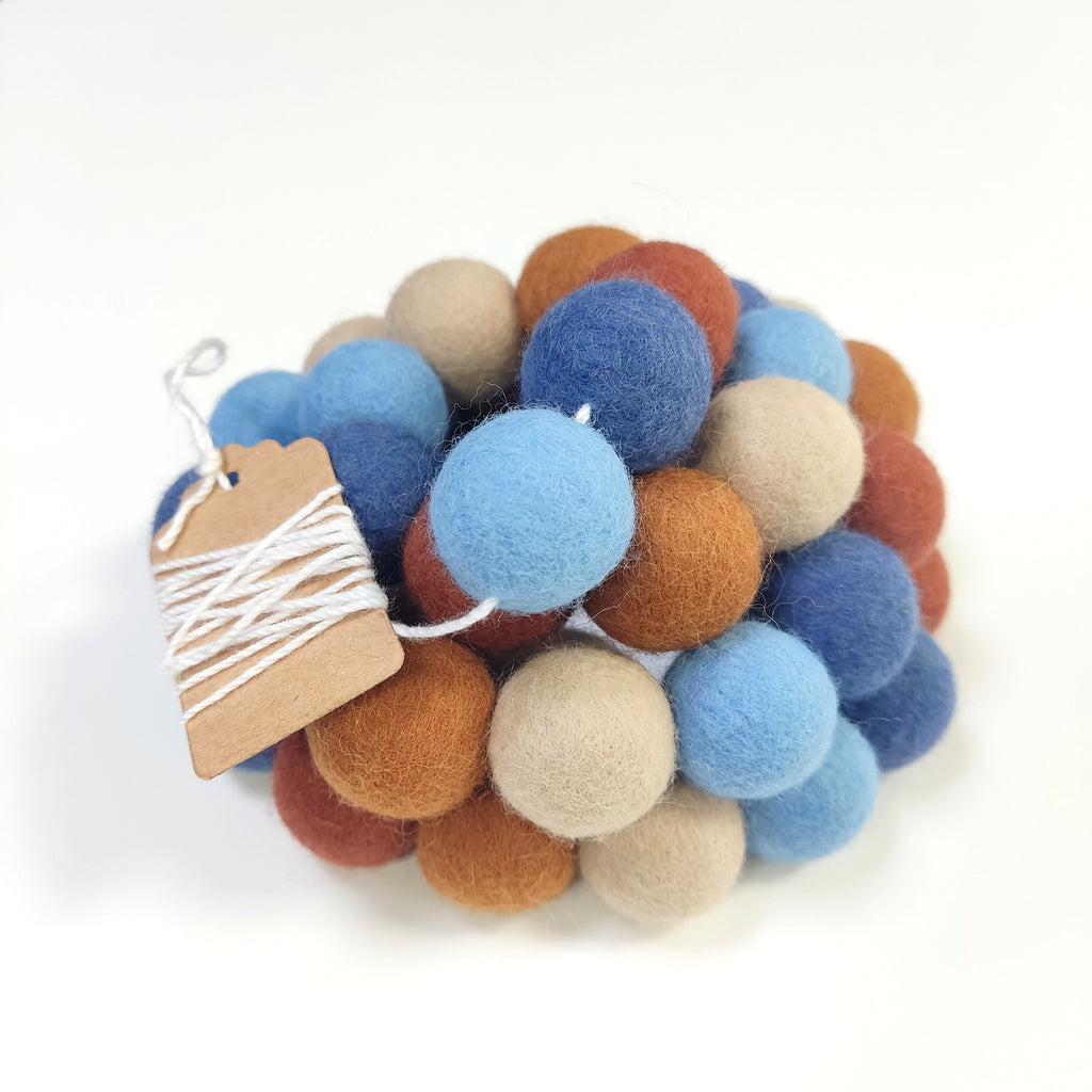 Zoom sur la guirlande de pompons en laine mérinos terracotta bleu beige avec son étiquette