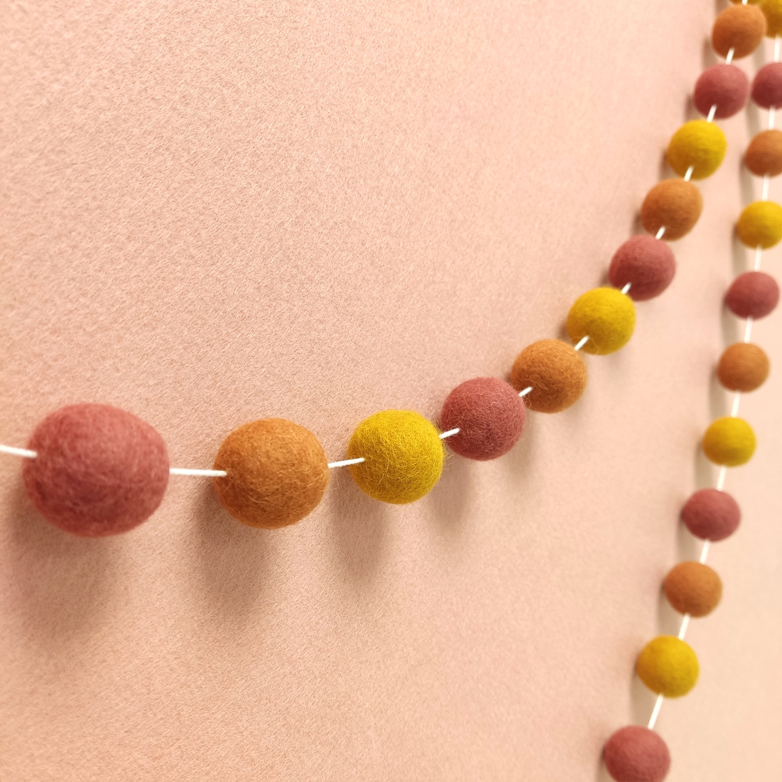 Guirlande de pompons feutrés aux teintes minérales terracotta rosé, terracotta cuivré et jaune ocre vue de profil