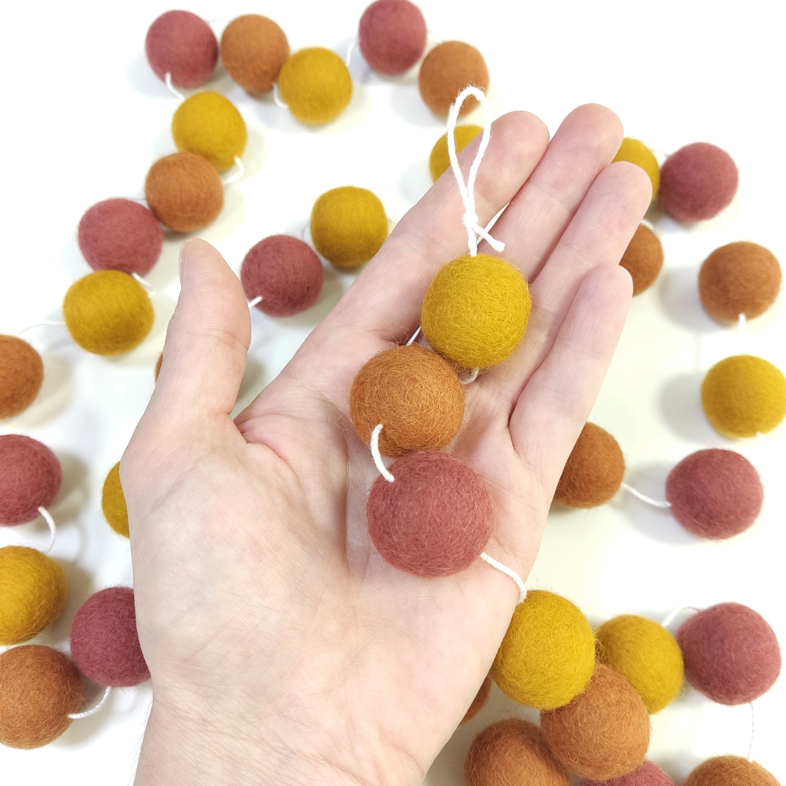 Zoom sur les pompons en laine mérinos terracotta ocre dans une main, teintes chaudes et naturelles