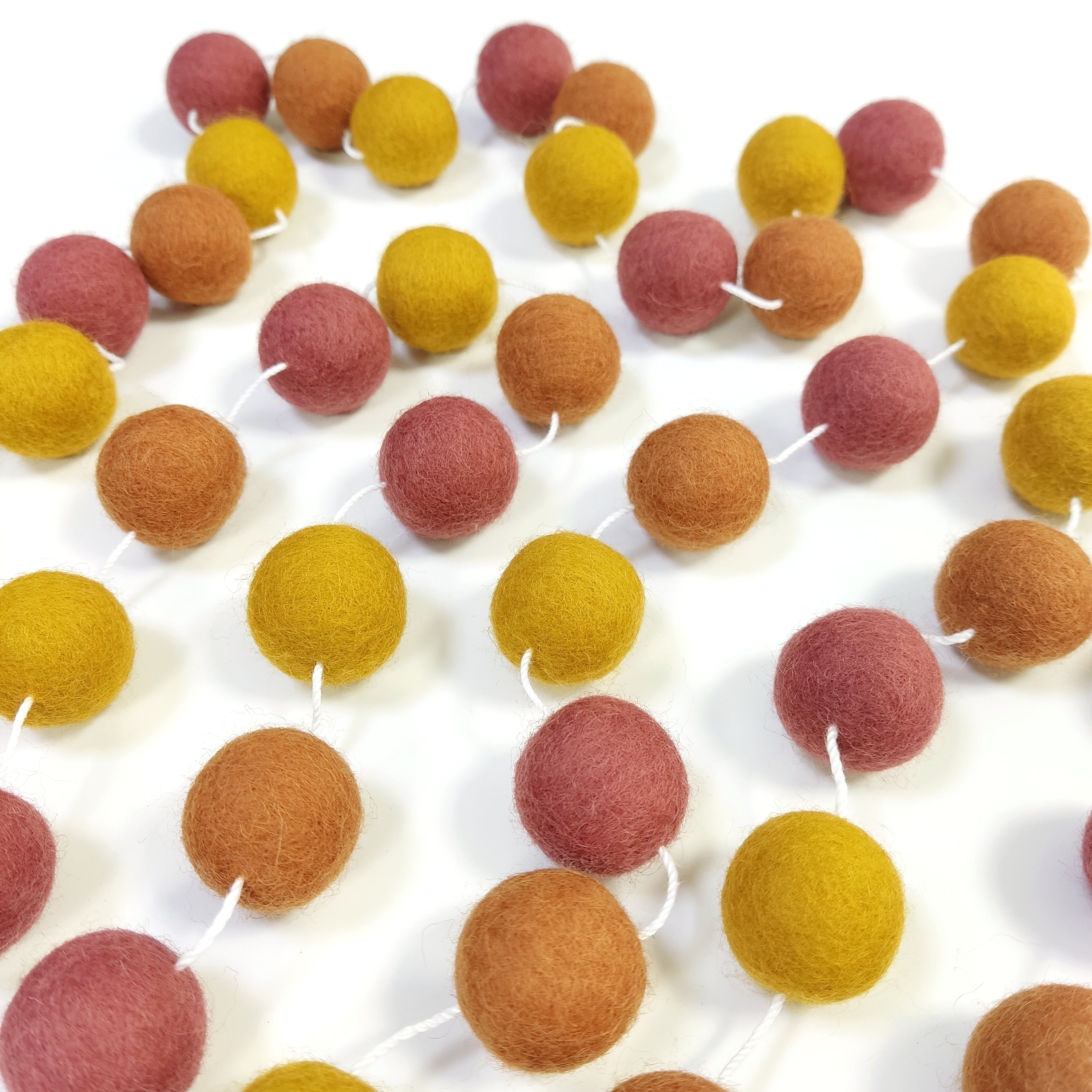 Guirlande de pompons feutrés terracotta ocre étalée sur une table avec les pompons espacés sur le fil