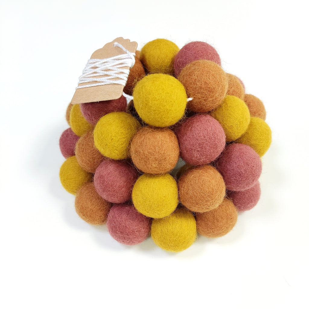 Zoom sur la guirlande de pompons en laine mérinos terracotta ocre avec étiquette CELAINEDECO