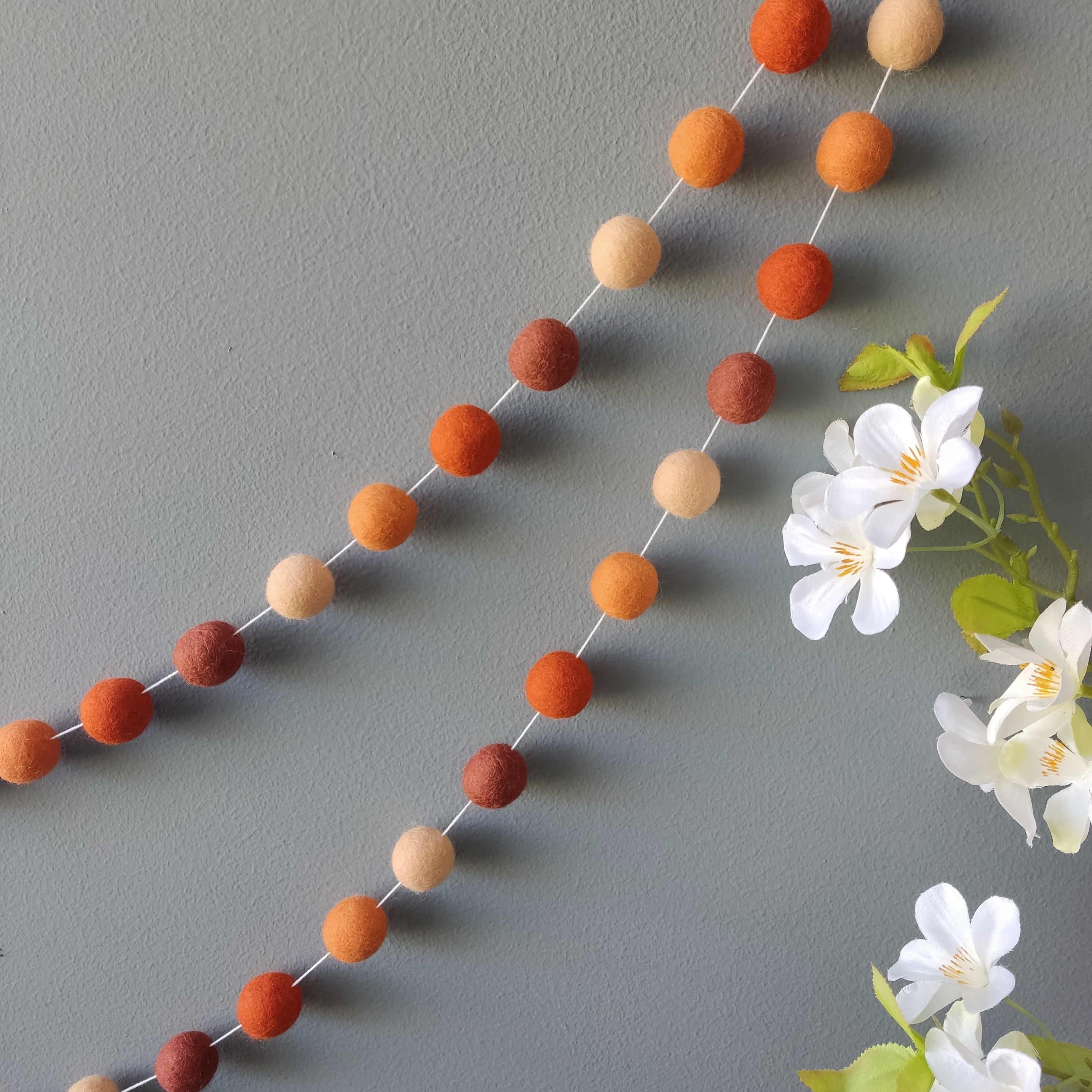 Guirlande de pompons feutrés tons terracotta et orange fixée au mur