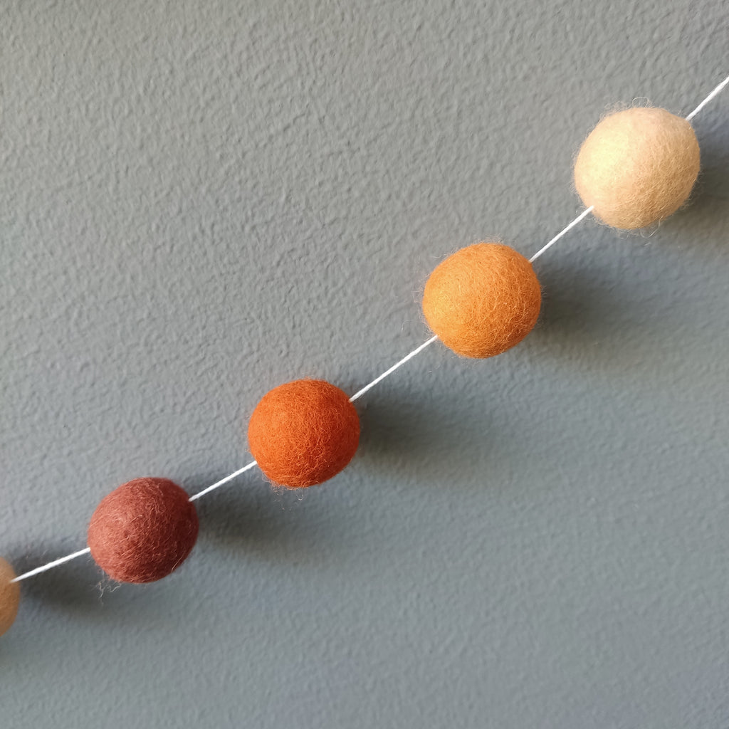Zoom sur les 4 couleurs des pompons en laine mérinos de la guirlande terracotta orange