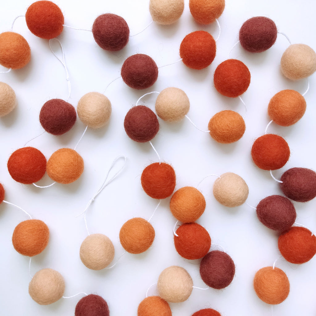 Guirlande de pompons feutrés terracotta orange étalée sur une table avec les pompons espacés