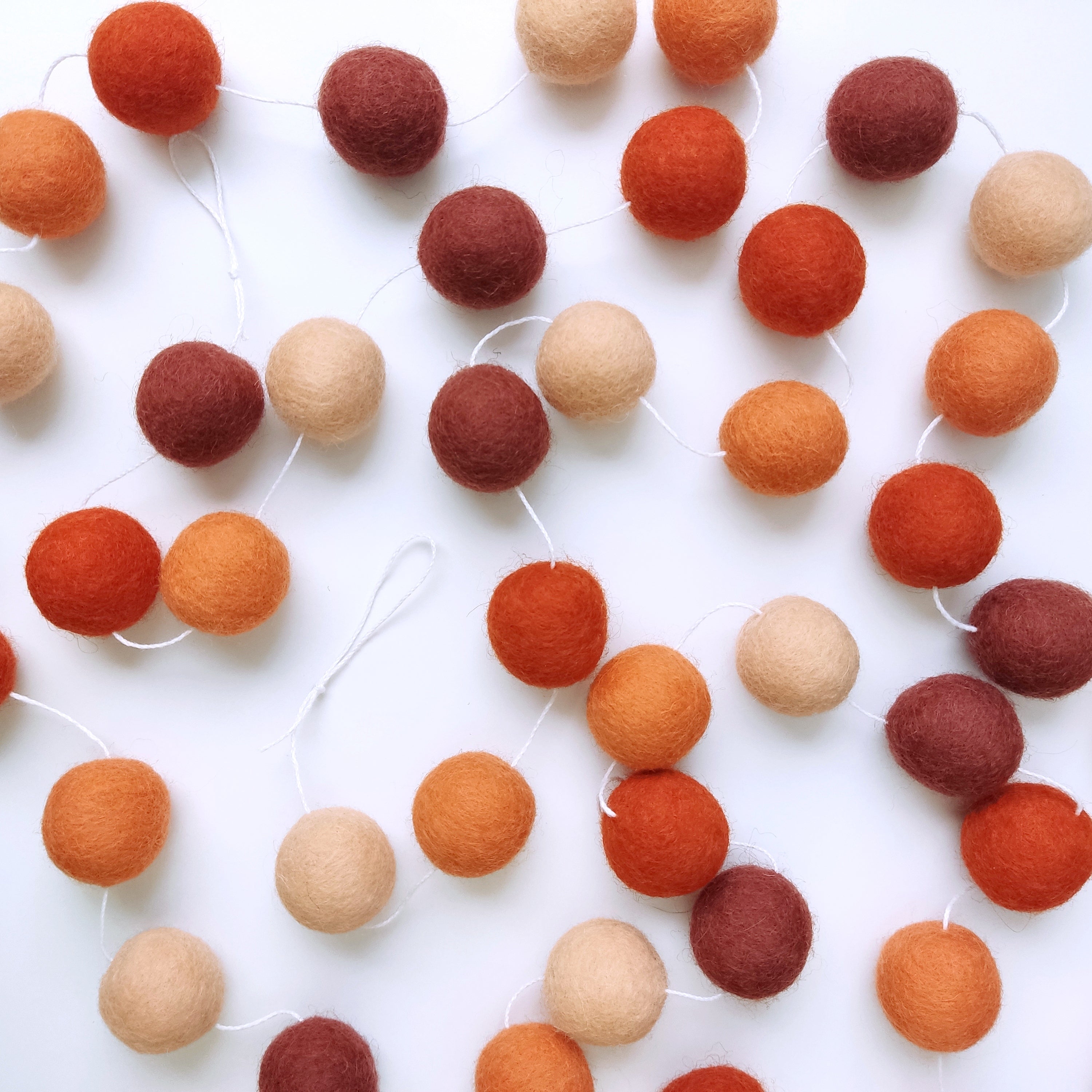 Guirlande de pompons feutrés terracotta orange étalée sur une table avec les pompons espacés