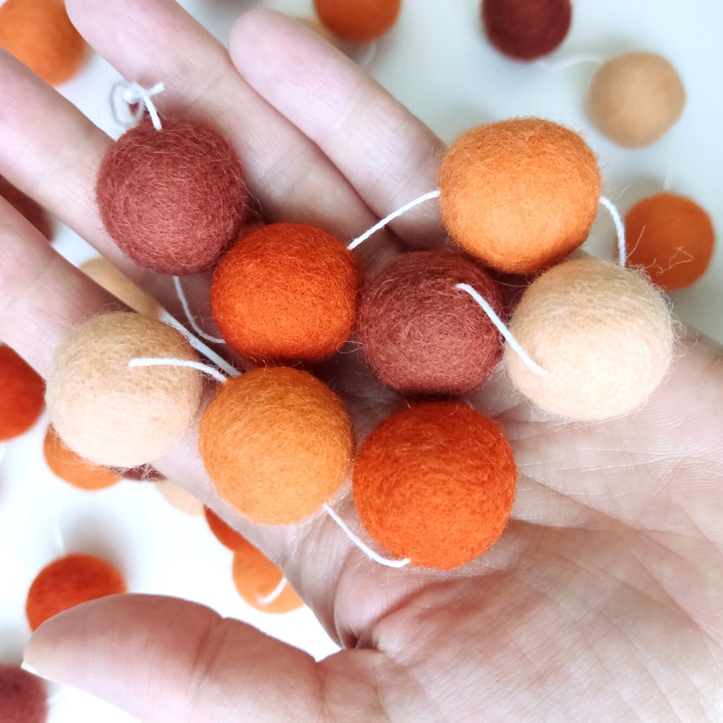 Pompons en laine feutrée 2, 5 cm de la guirlande terracotta orange dans une main