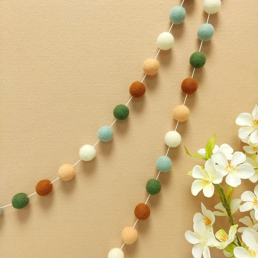 Guirlande de pompons feutrés pour décoration cosy aux couleurs terracotta, pêche, blanc et vert