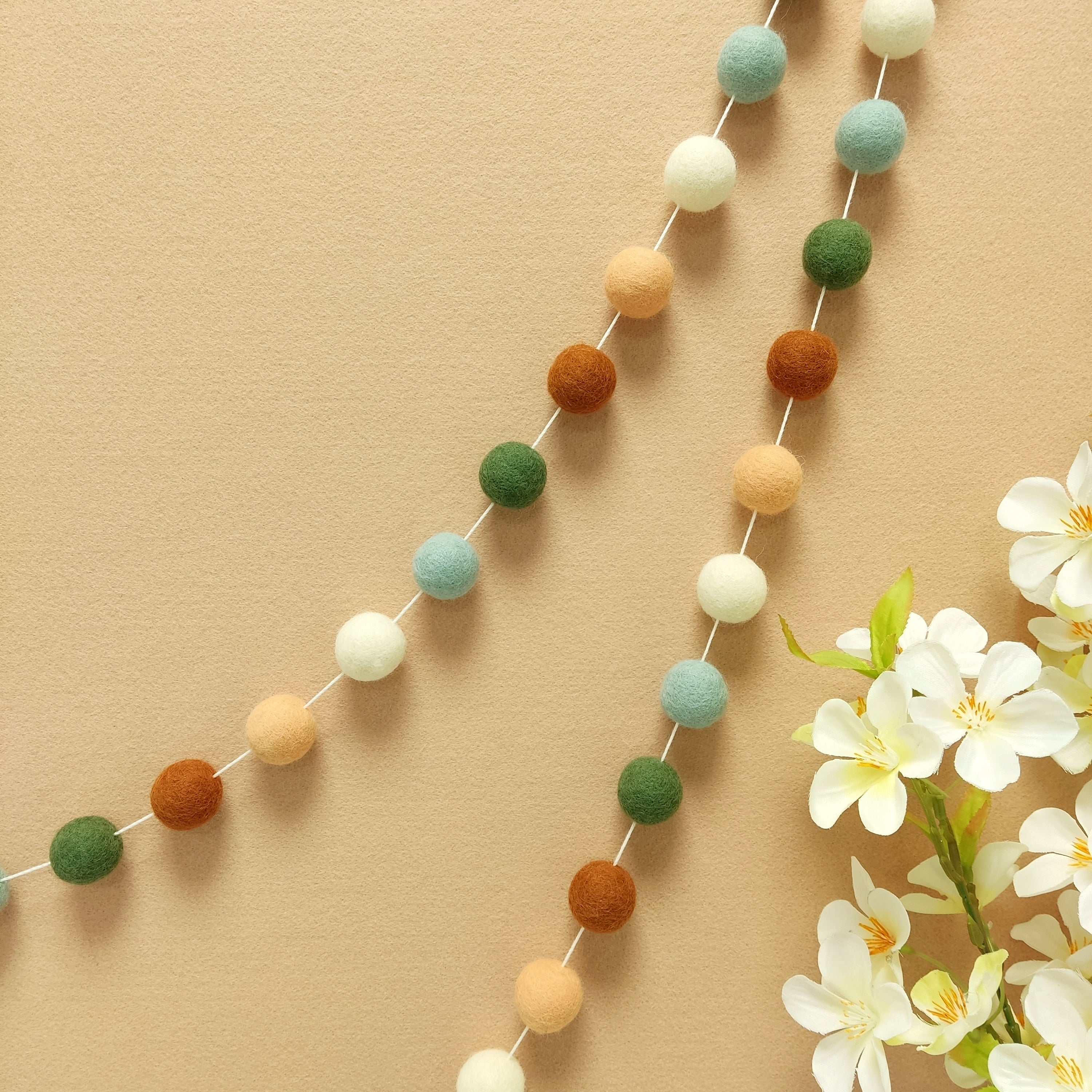 Guirlande de pompons feutrés pour décoration cosy aux couleurs terracotta, pêche, blanc et vert