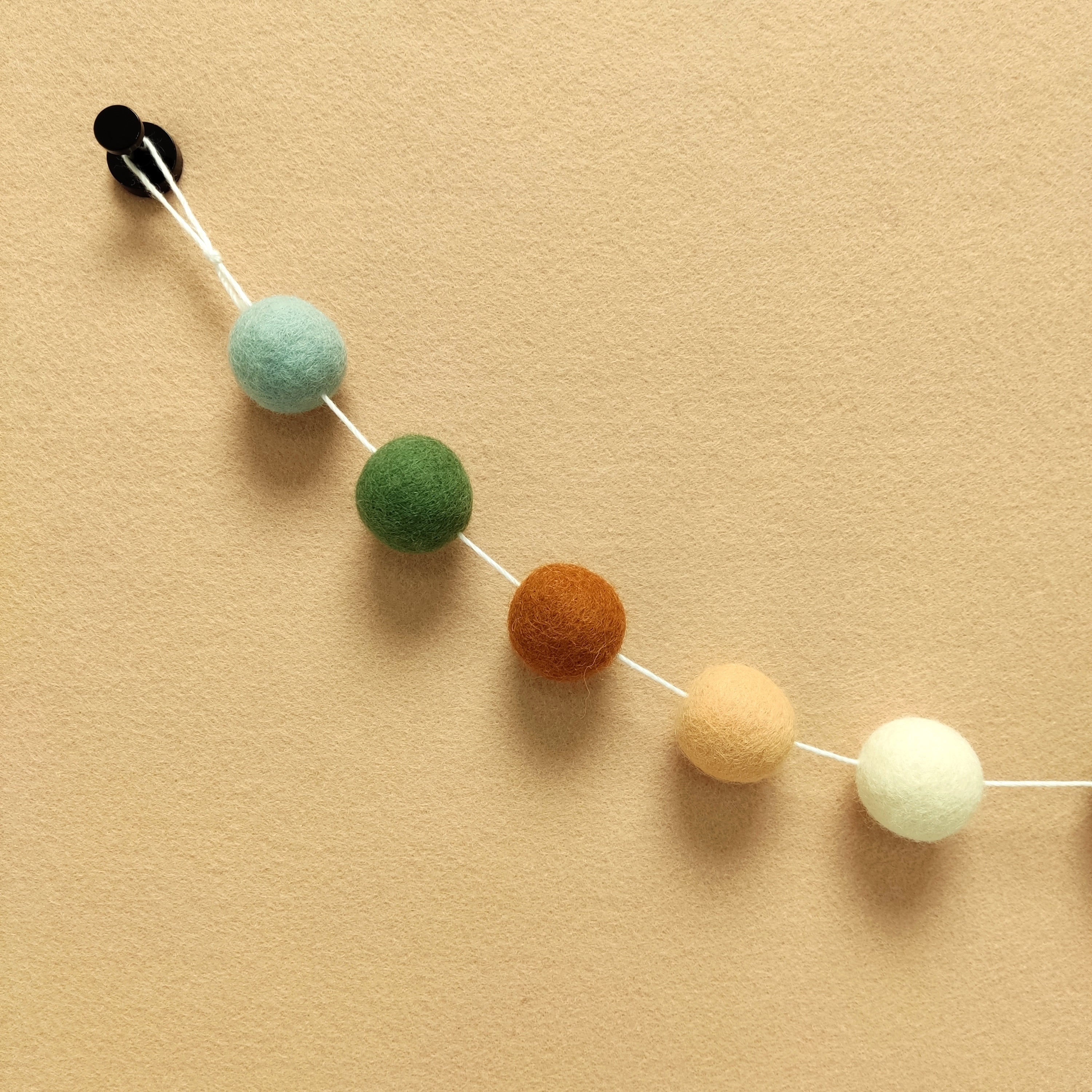 Zoom sur les 5 couleurs de la guirlande terracotta sauge en boules de feutre terracotta cuivre, vert matcha, orange pêche, blanc et vert céladon
