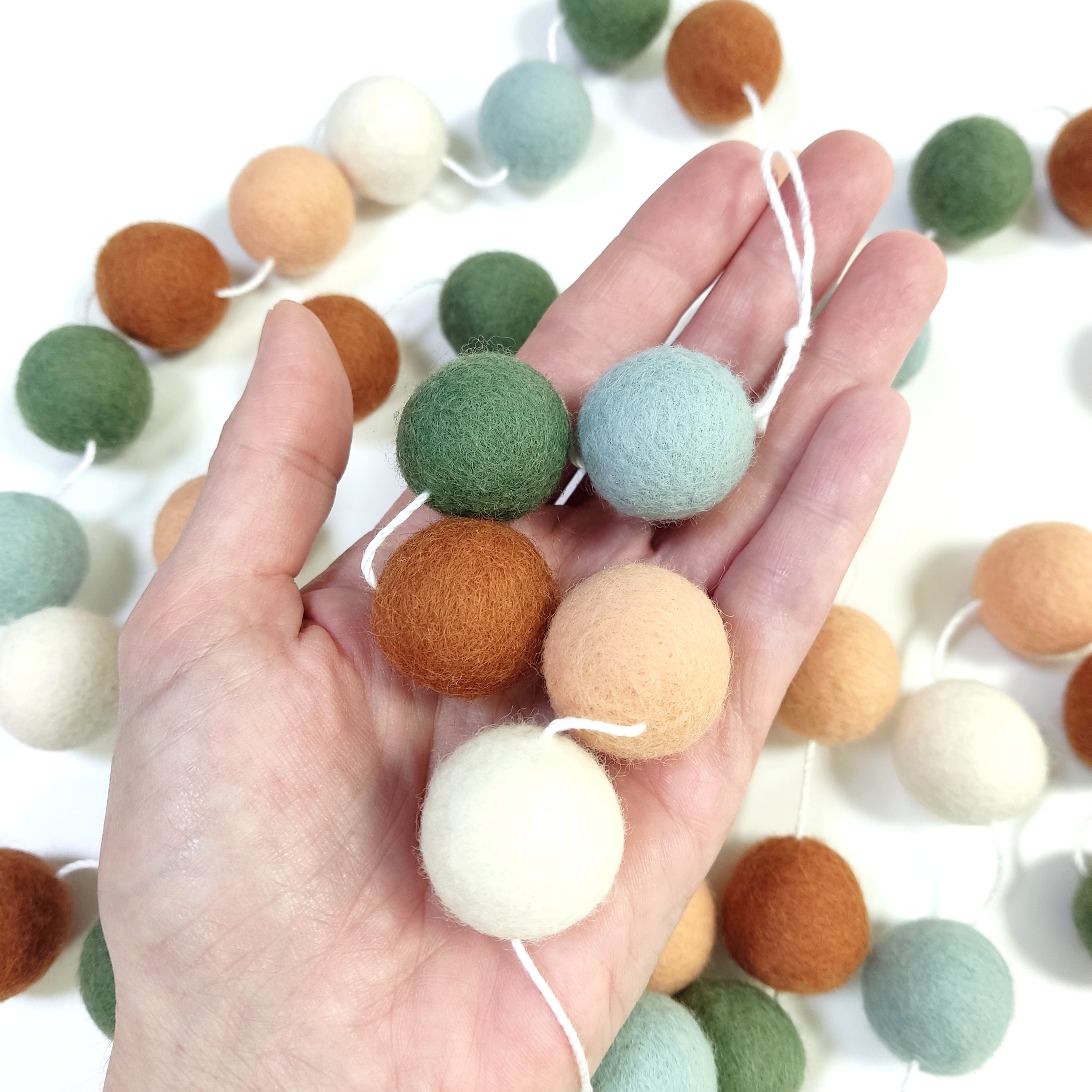 Zoom sur les pompons de feutre terracotta, vert céladon, blanc et vert matcha de 2,5 cm dans une main