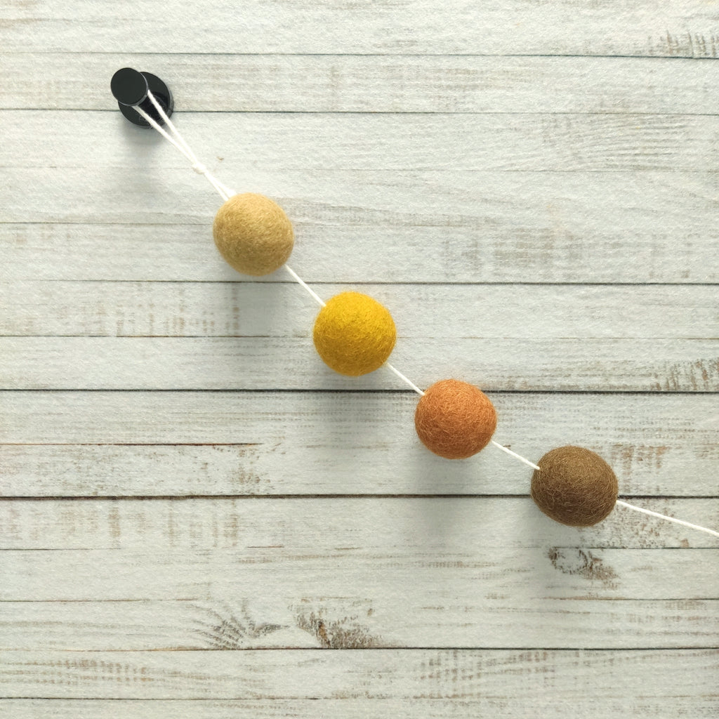 Zoom sur les 4 couleurs de la guirlande en boules de feutre terracotta, ocre, beige et noisette