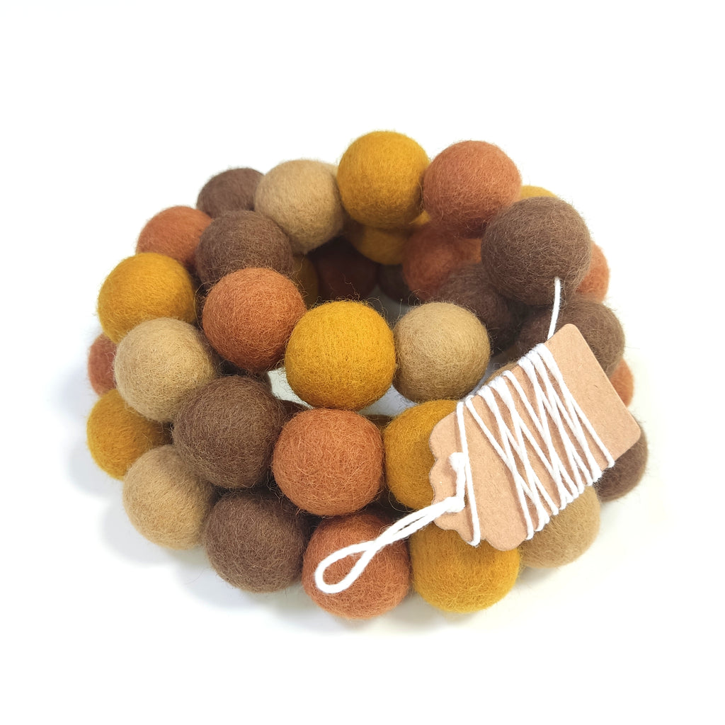 Guirlande terre et ocre avec pompons rassemblés sur le fil et enroulée sur elle-même