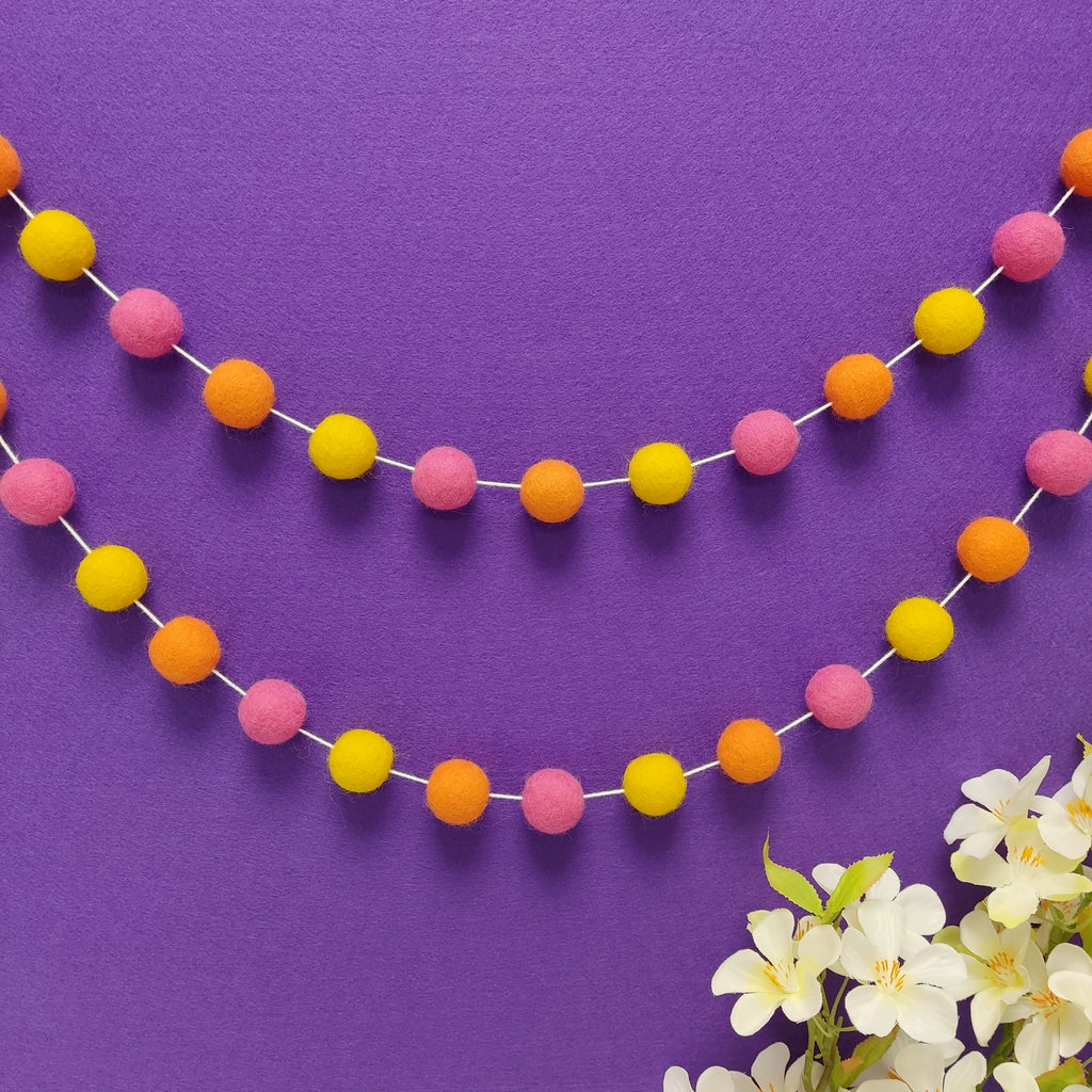 Guirlande de pompons en laine mérinos tutti frutti fixée en arc de cercle sur un mur, faite main en France