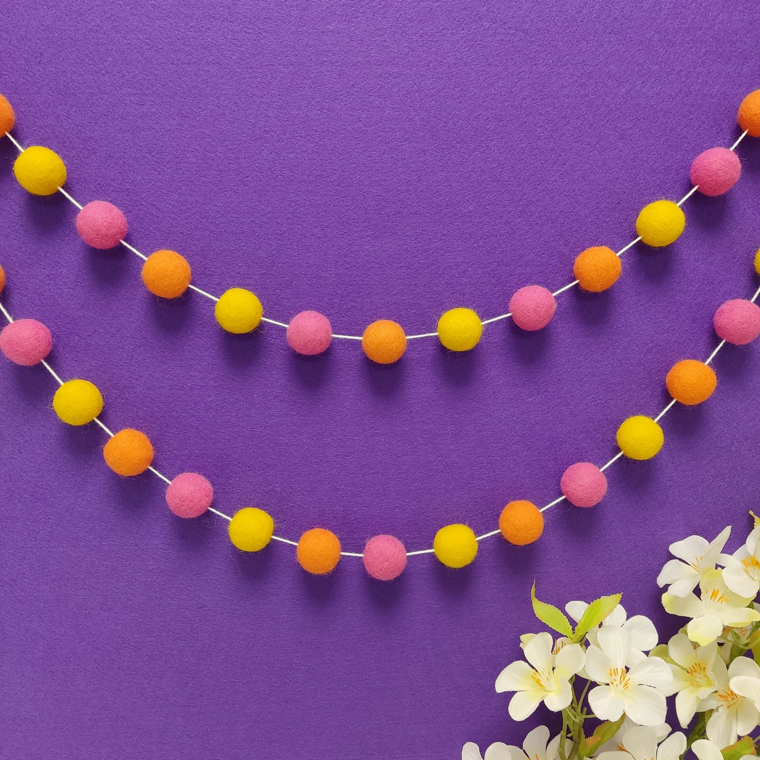 Guirlande de pompons en laine mérinos tutti frutti fixée en arc de cercle sur un mur, faite main en France