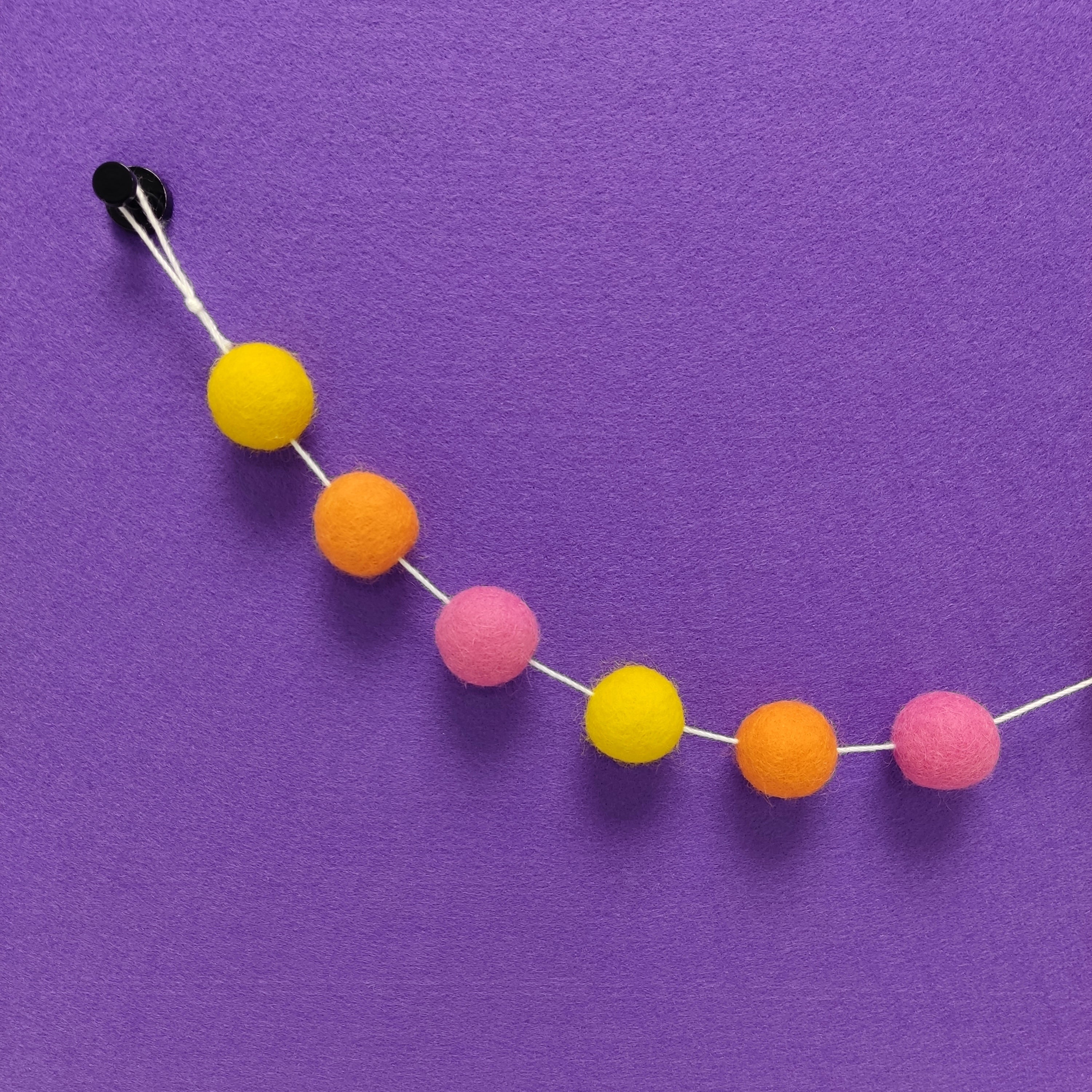 Détail des 3 couleurs de pompons feutrés rose bonbon, orange carotte et jaune soleil de la guirlande Tutti Frutti
