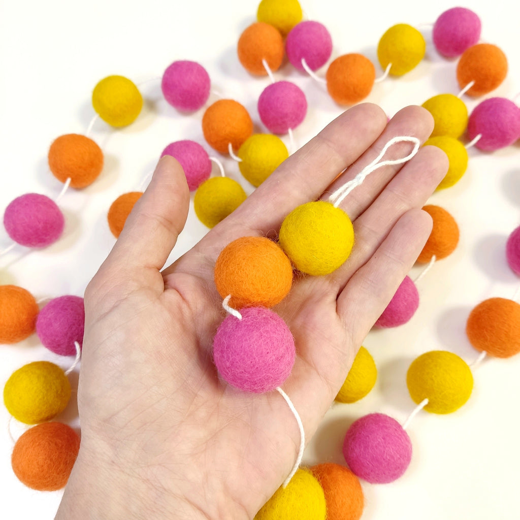 Zoom sur les pompons en laine mérinos tutti frutti dans une main, teintes vives et estivales
