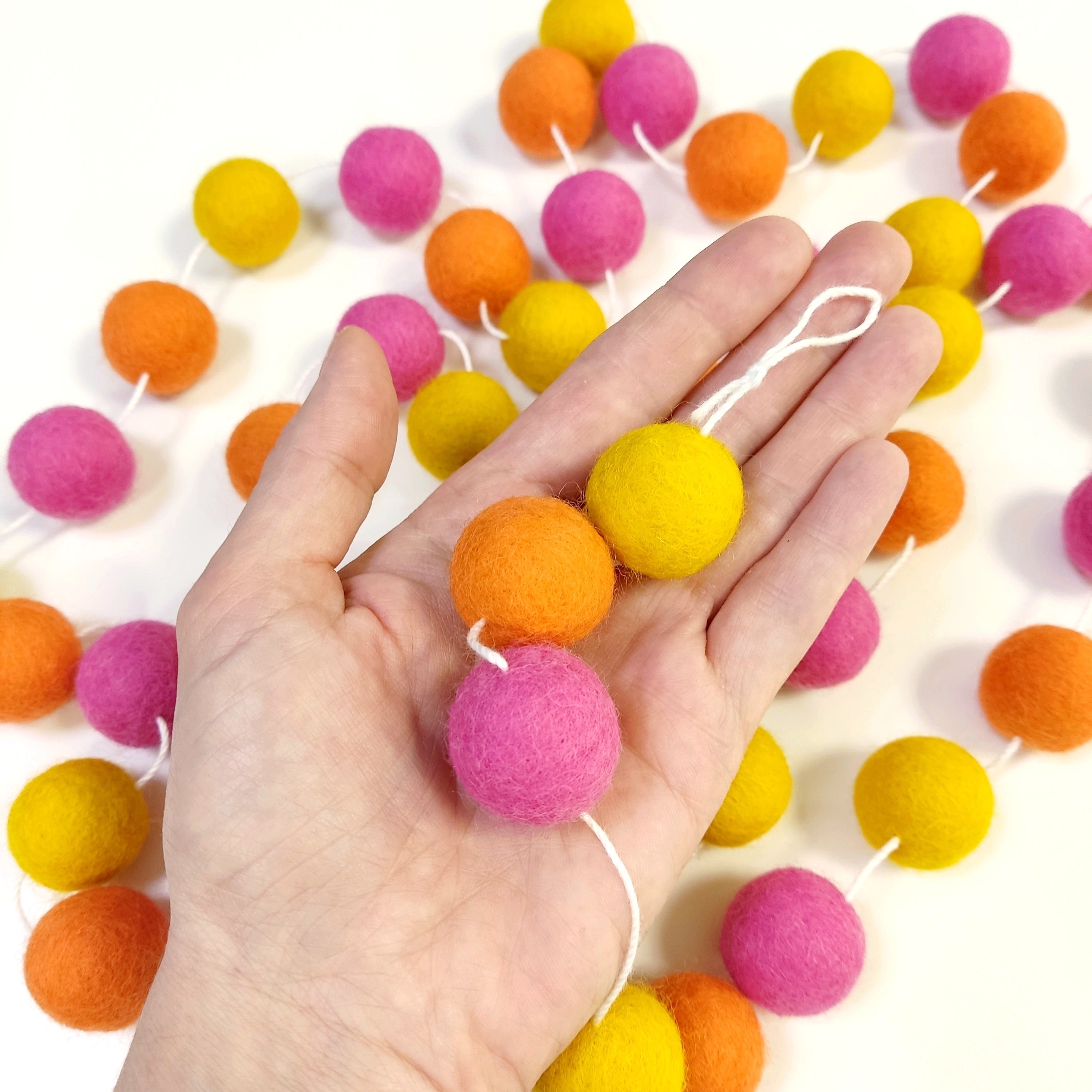 Zoom sur les pompons en laine mérinos tutti frutti dans une main, teintes vives et estivales
