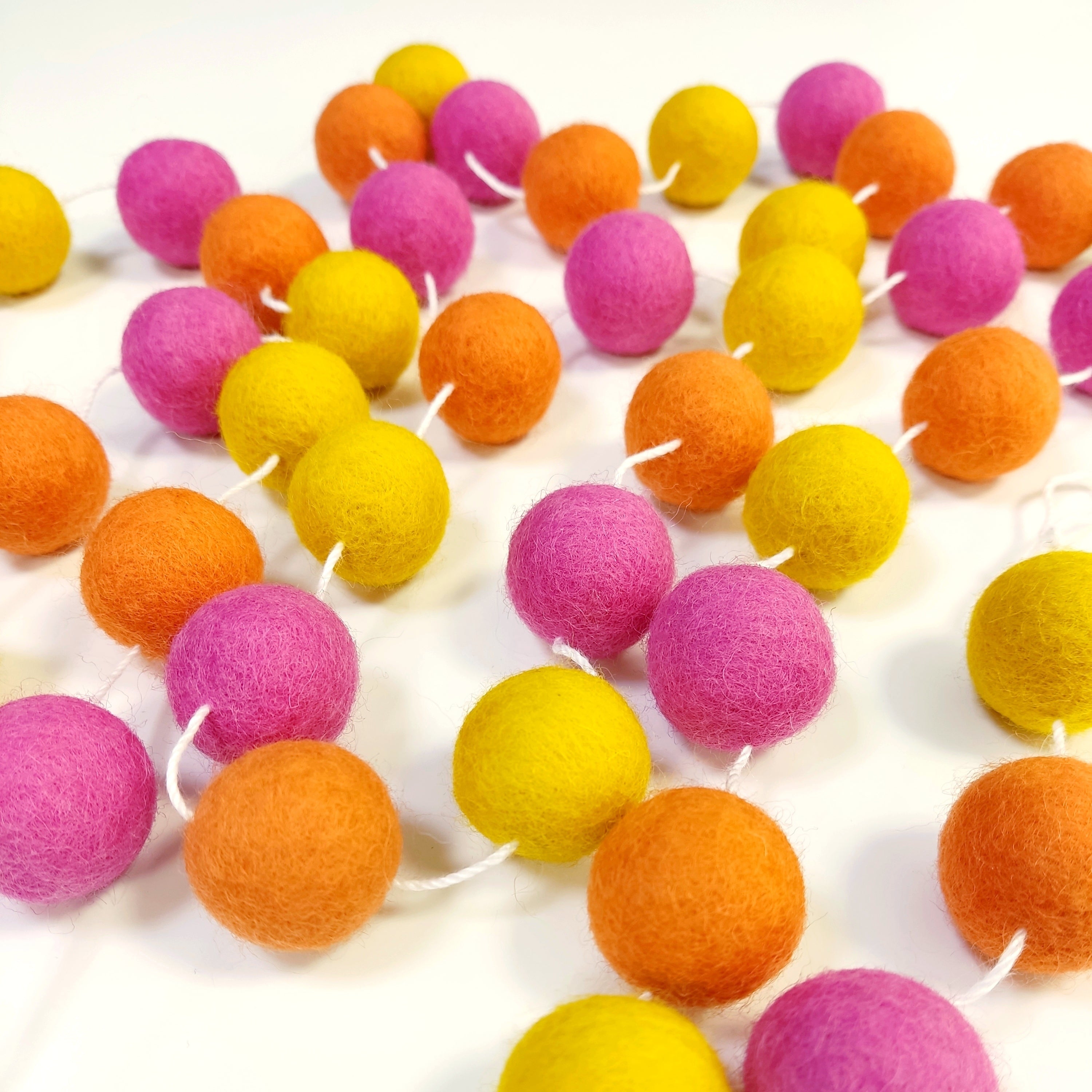 Guirlande de pompons feutrés tutti frutti étalée sur une table avec les pompons espacés sur le fil