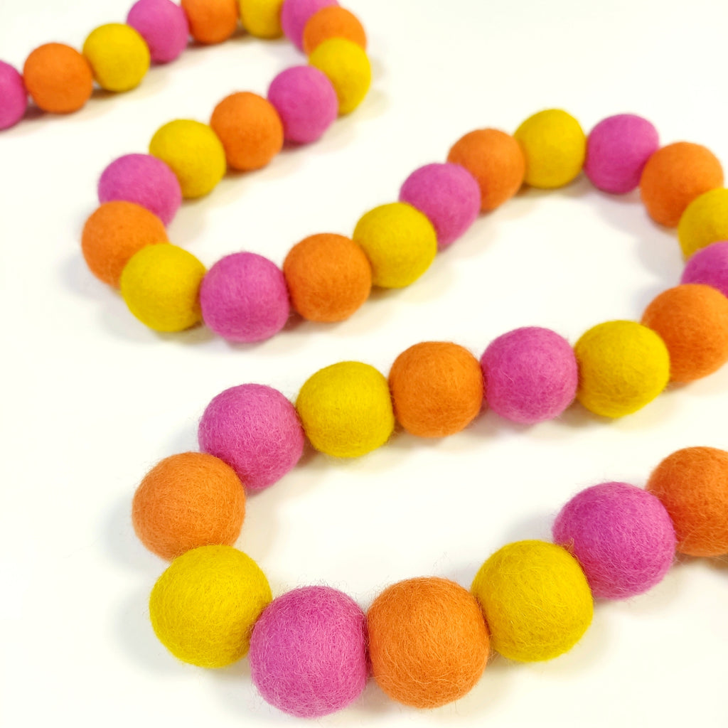 Guirlande en boules de feutre tutti frutti disposée en serpentin sur une table