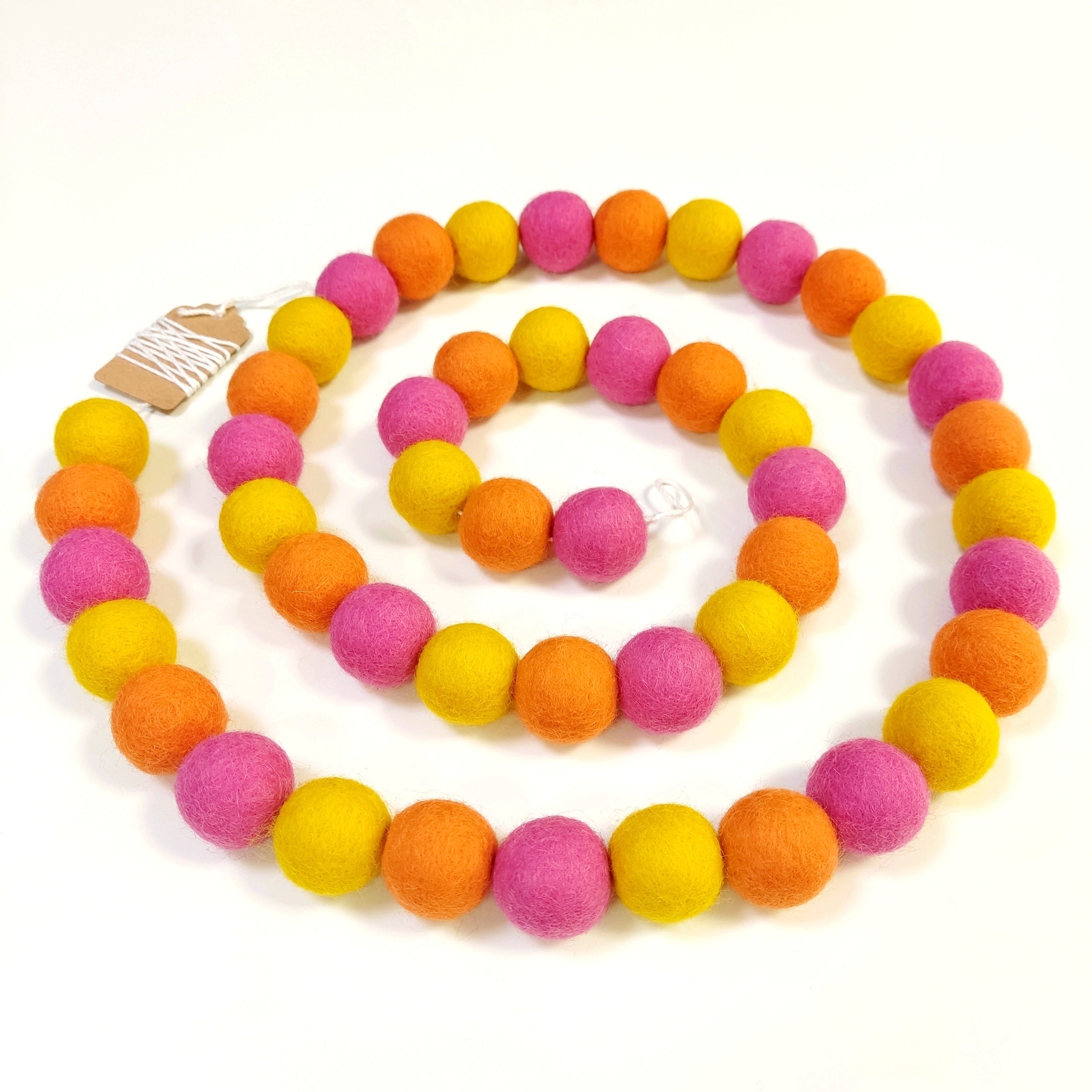 Guirlande de pompons feutrés tutti frutti disposée en spirale sur fond blanc