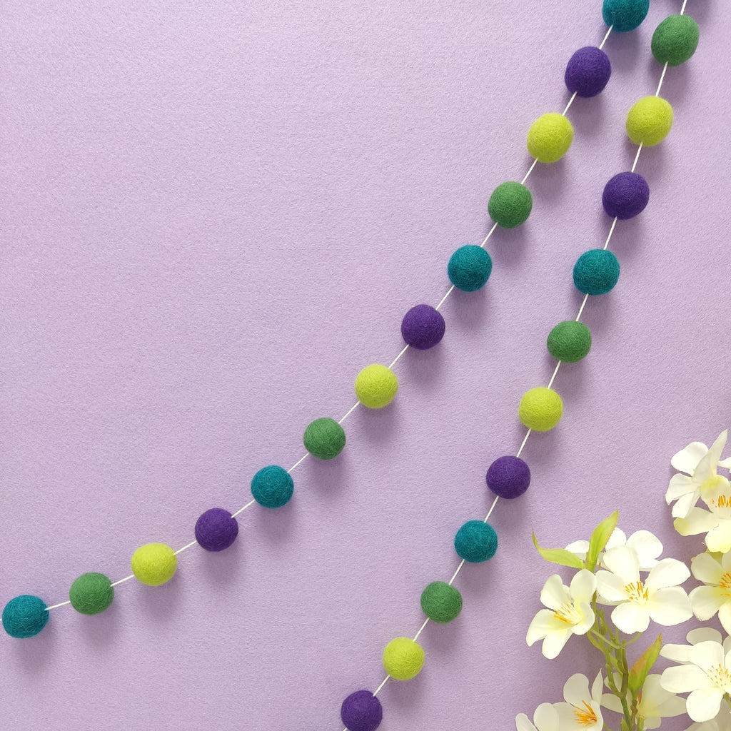 Guirlande de pompons feutrés vert et violet suspendue sur un mur, faite main en France — CELAINEDECO